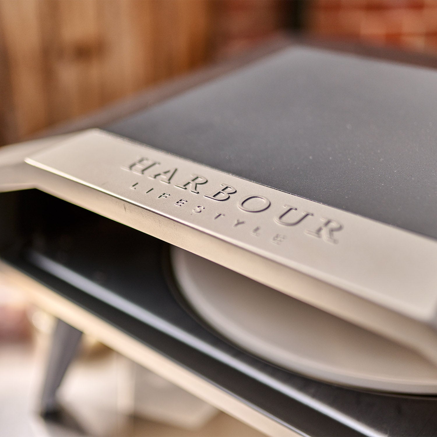 Close-up of the Juno 16" Pizza Oven Bundle with Stainless Steel Pizza Peel, engraved with "Harbour Lifestyle" on its surface, featuring foldable legs and a built-in heat gauge thermometer.