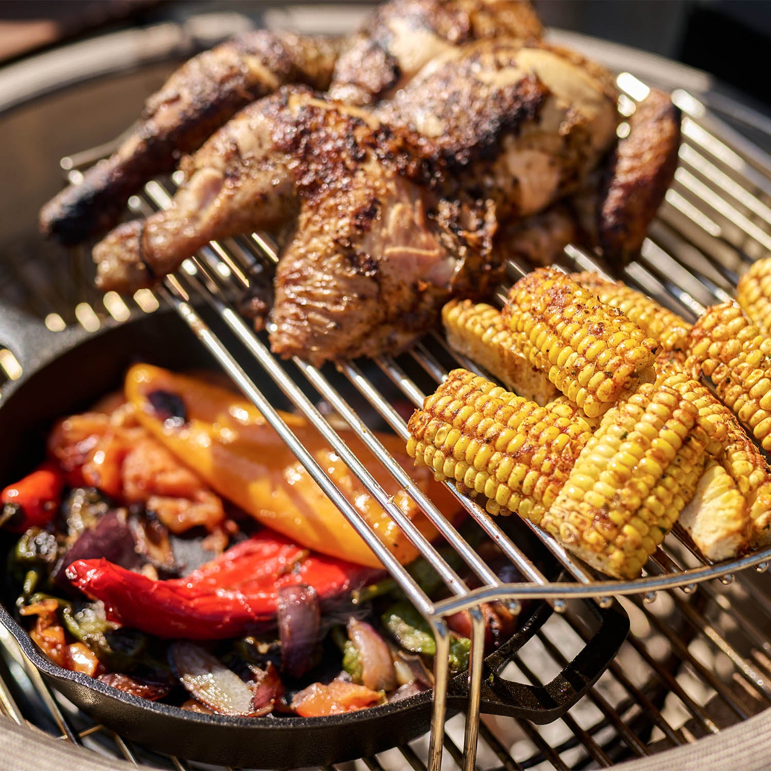 Grilled chicken, corn on the cob, and assorted vegetables sizzle on a Kamado Grill with a Cooking Grid Expander for 18" Kamado Grills, providing 60% more cooking space.