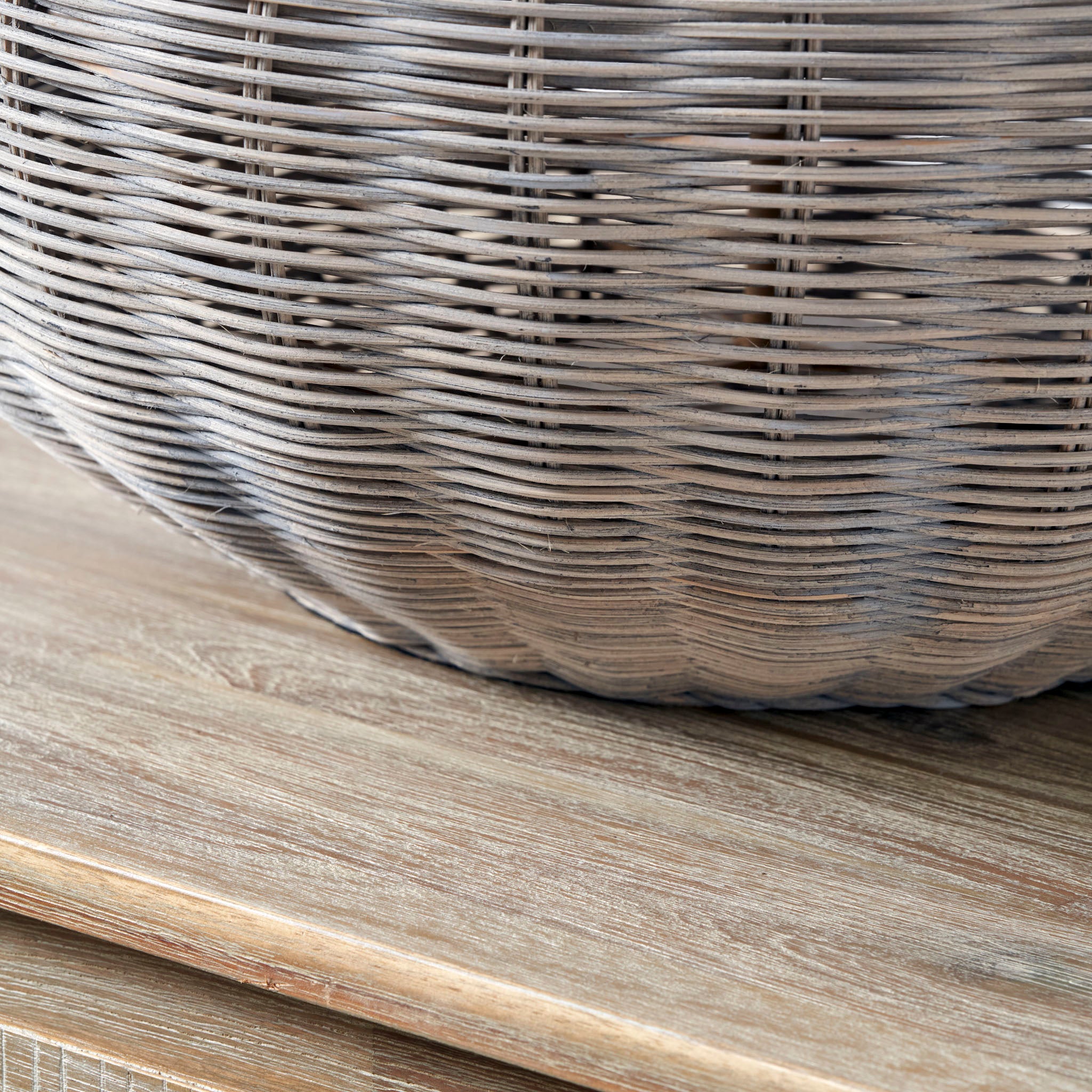 Close-up of the Pacific Lifestyle Allona Grey Wash Rattan Table Lamp, showcasing its textured weave and organic tactile finish on a wooden surface.