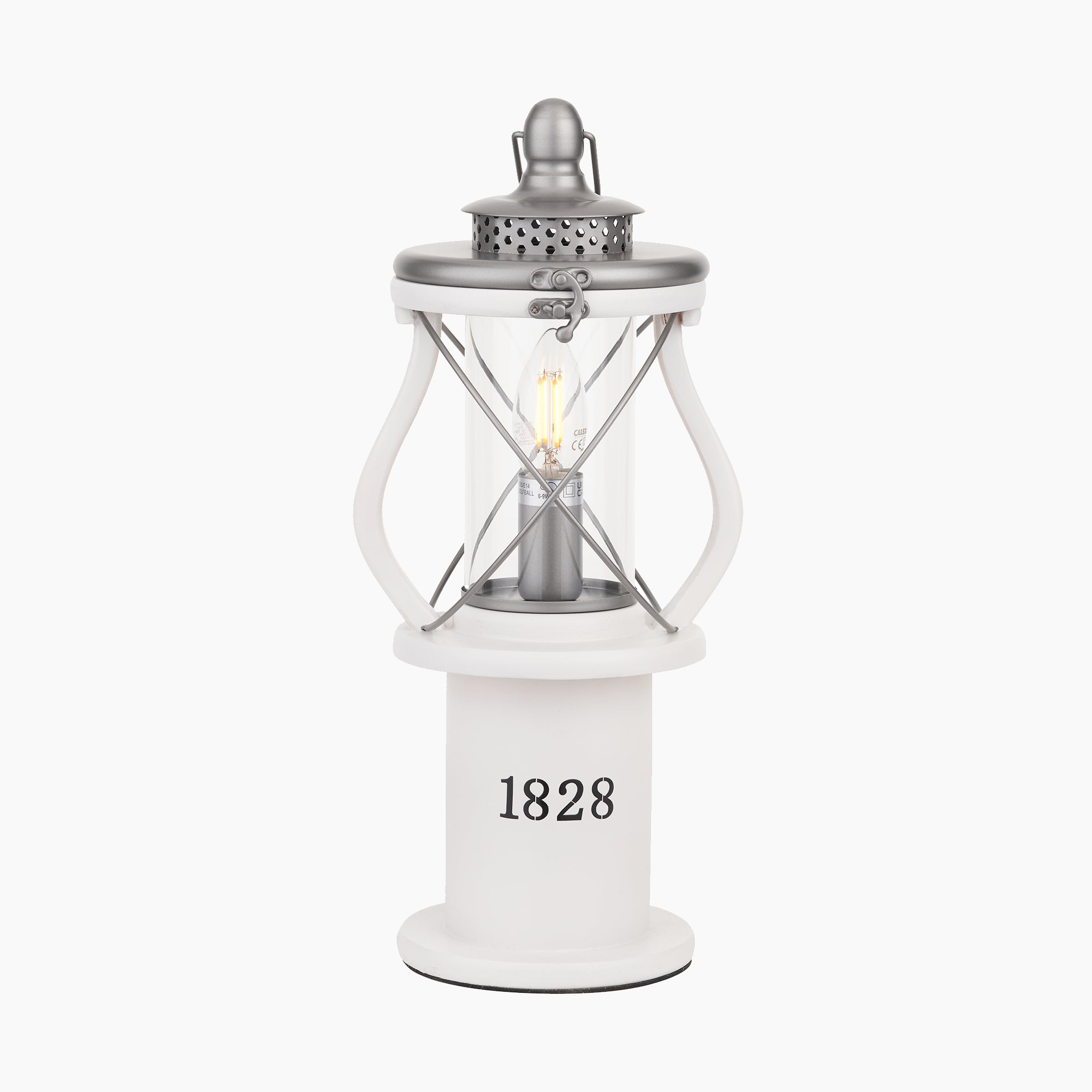 The Pacific Lifestyle - Gibson Wood Lantern Table Lamp in White Wood features a metallic top, clear glass panels, and a cylindrical base with "1828" print—bringing timeless Victorian charm to any room.