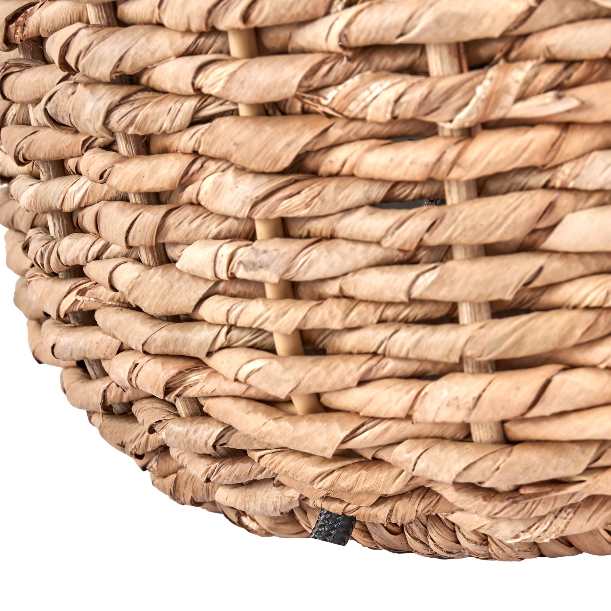 A close-up of the Pacific Lifestyle Acer Natural Woven Small Table Lamp in Ivory reveals tightly braided natural wicker fibers and a small black fabric tag, exuding a rustic look similar to an ivory jute shade.