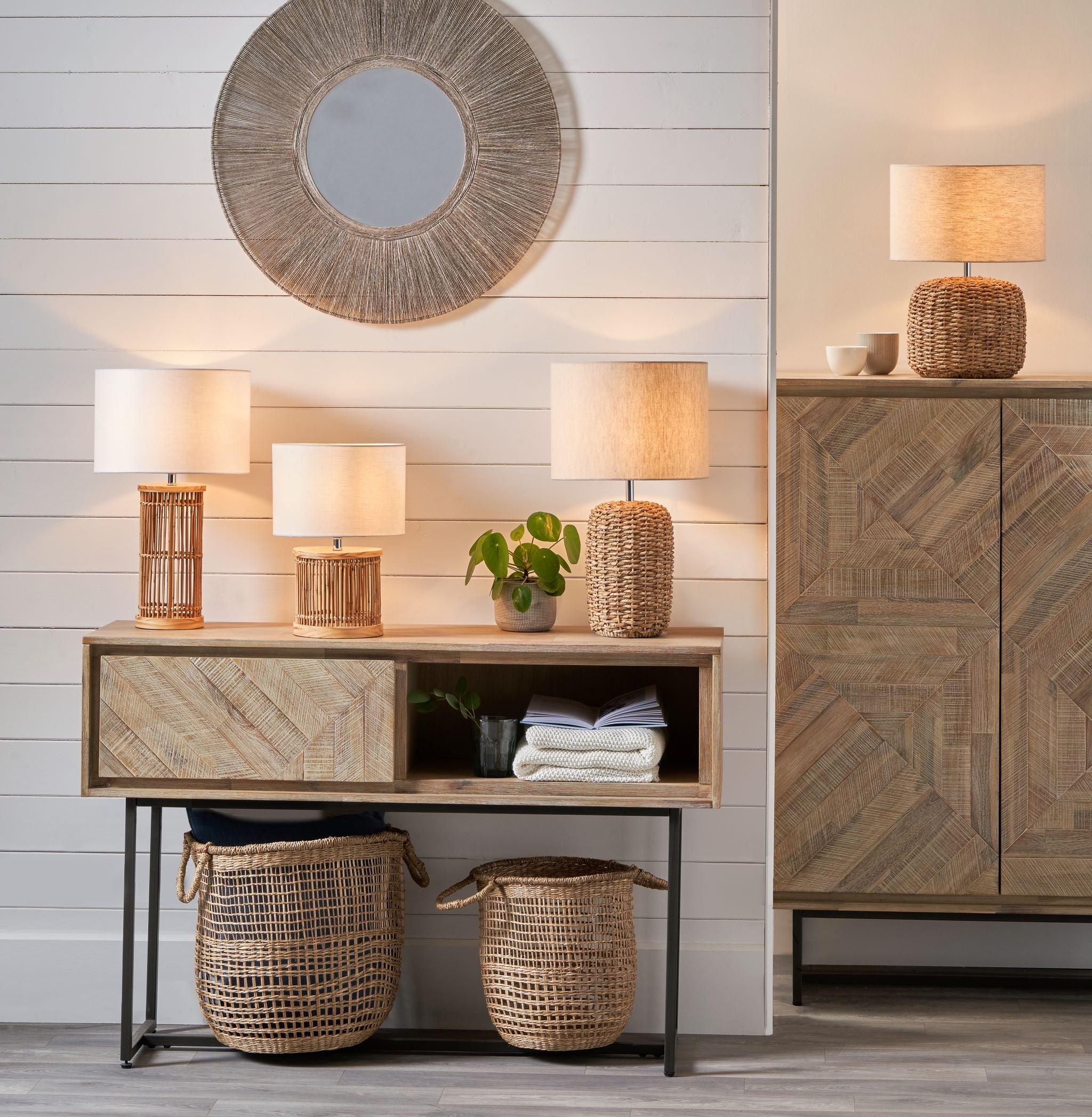 Rustic room with wood furniture, wicker baskets, and the Pacific Lifestyle - Acer Natural Woven Tall Table Lamp in Ivory. A circular mirror is elegantly mounted on the shiplap wall, exuding warmth with neutral tones.