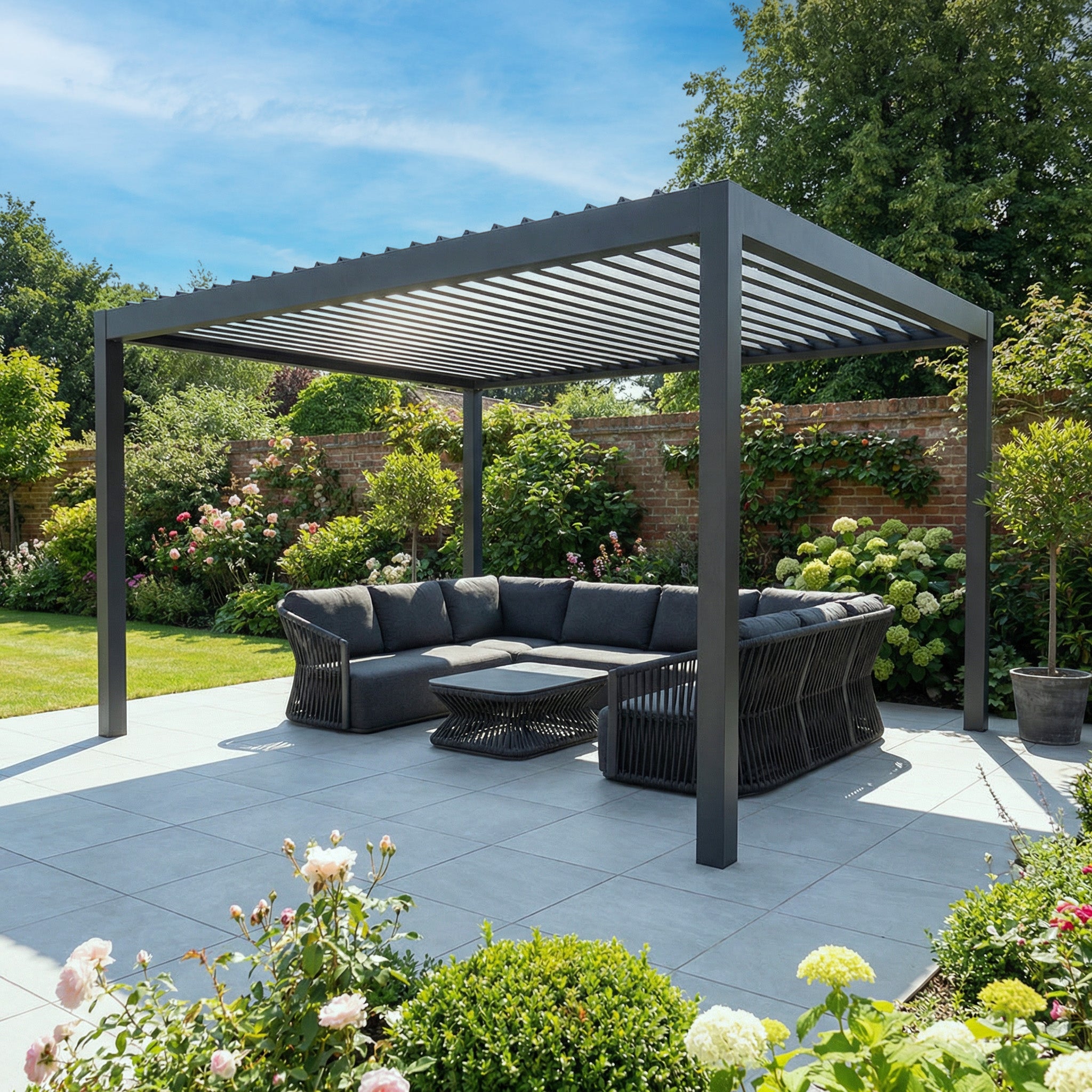 The PergoSTET Deluxe 3m x 4m Grey Pergola features motorised LED louvres, set on a tiled patio with a black sofa and lush garden surrounds.