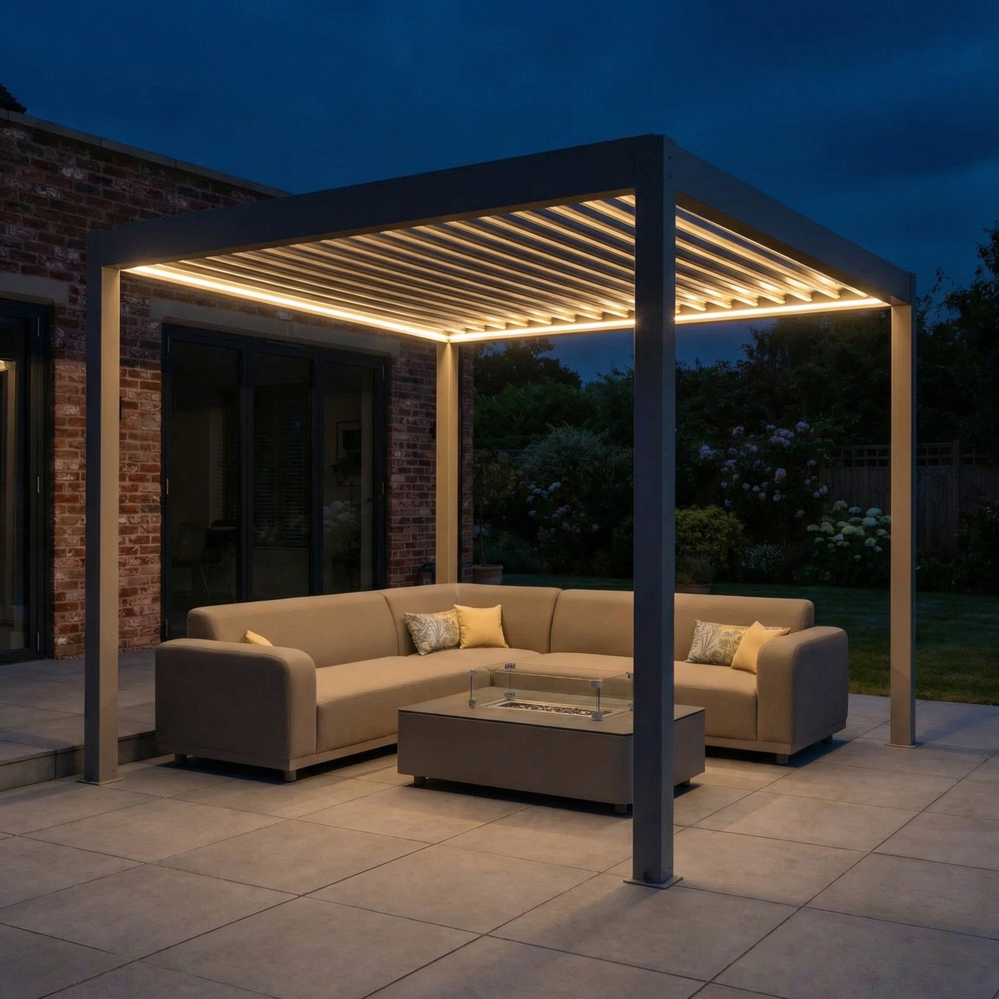 Modern outdoor patio with a lit PergoSTET Plus Frame Only 3m x 3m Square Pergola in Latte, waterproof roof, beige sofas, and glass coffee table at dusk.