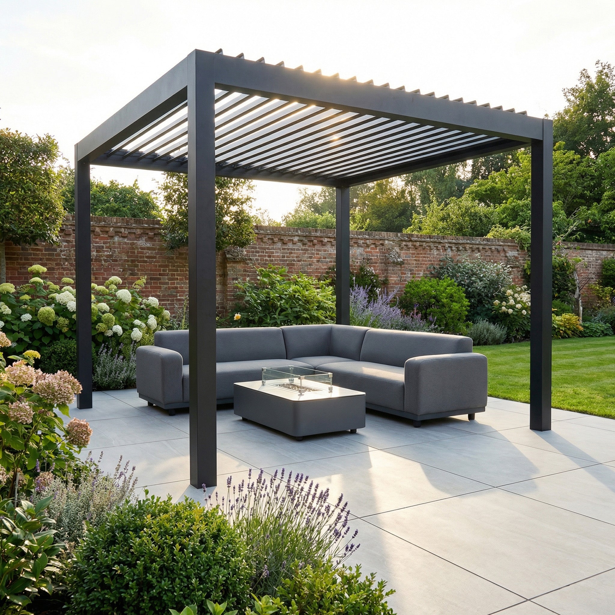 The PergoSTET Deluxe Frame Only 3m x 3m Square Pergola features motorised LED louvres in grey, creating a modern outdoor space with sectional sofa and table on a patio, surrounded by lush garden greenery.