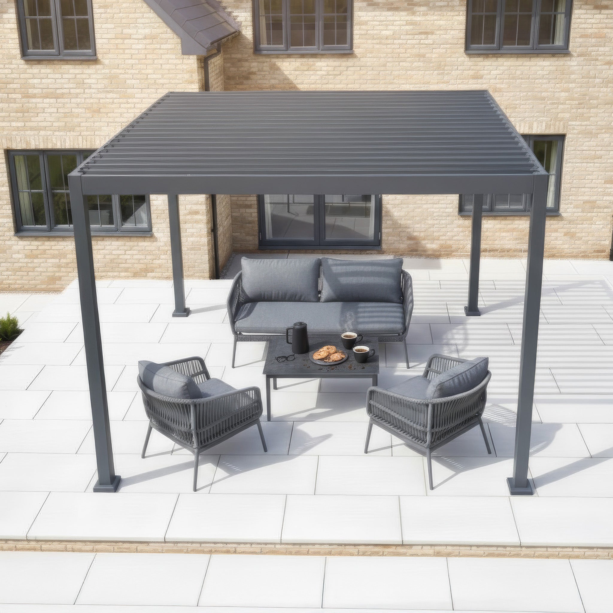 PergoSTET Lite 3m x 3m Metal Square Pergola in Grey with tilting louvres, patio furniture, and snacks on a table, placed on a tiled patio outside a house.