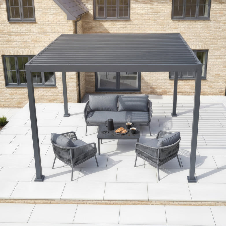 PergoSTET Lite 3m x 3m Metal Square Pergola in Grey with tilting louvres, patio furniture, and snacks on a table, placed on a tiled patio outside a house.