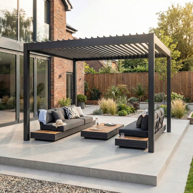 Modern patio with a PergoSTET Pro Frame Only 3m x 3m Square Pergola in Grey featuring LED lighting, gray outdoor sofas, low tables, and a landscaped garden in the background.