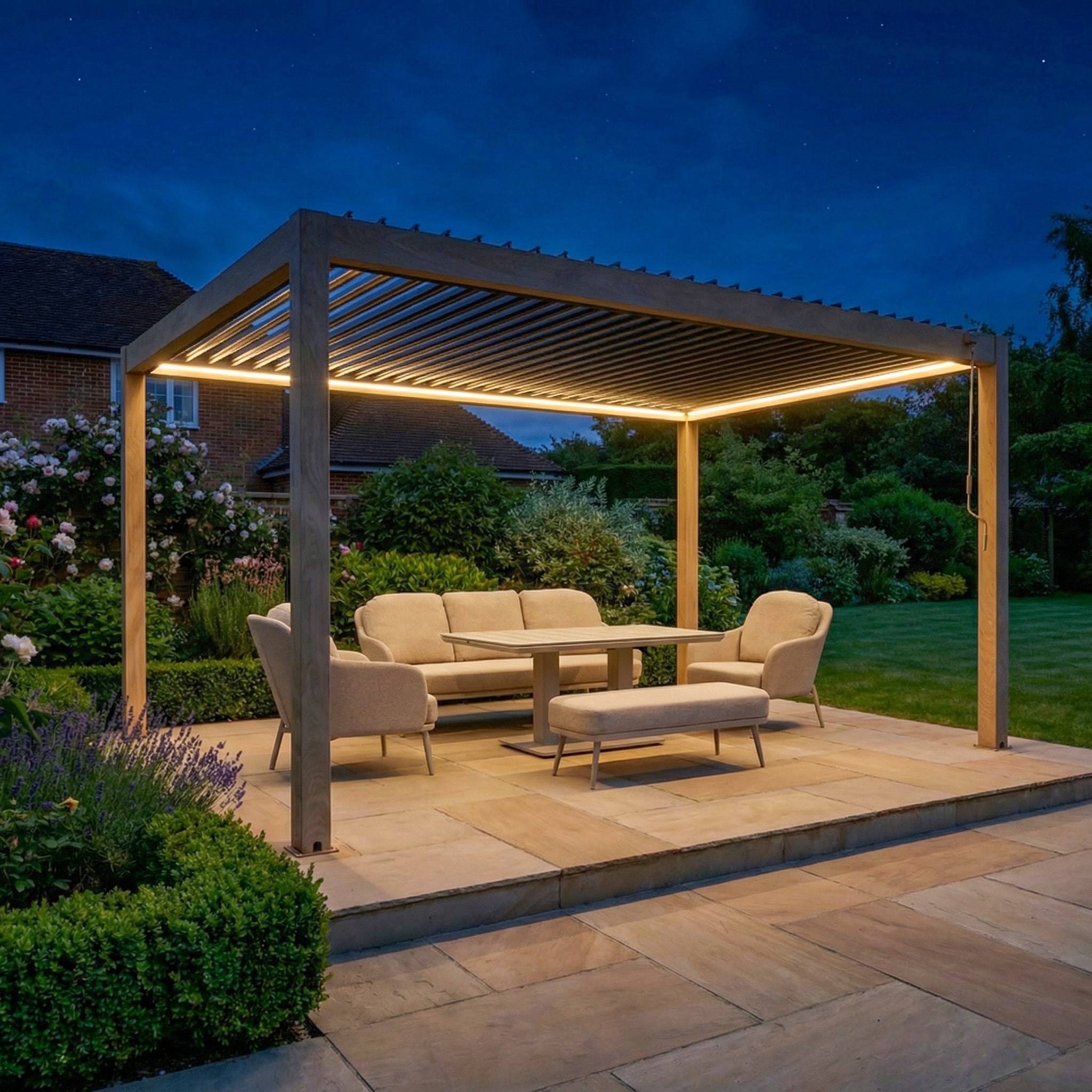 The PergoSTET Plus Frame Only 3m x 4m Rectangular Pergola with LED Lighting in Wood Effect shelters outdoor seating at dusk, its louvred roof and integrated LEDs enhancing ambiance in a landscaped backyard.