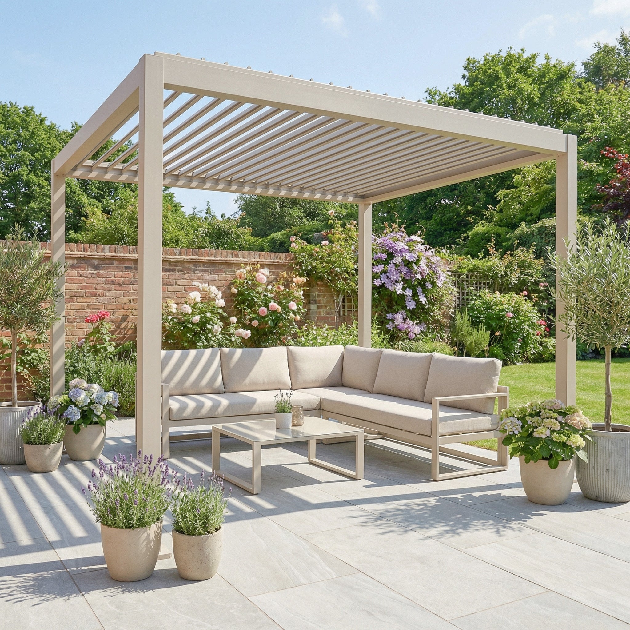 The PergoSTET Lite 3m x 3m Metal Square Pergola in Latte stands on a sunny patio, paired with a corner sofa and potted plants, surrounded by a lush garden.