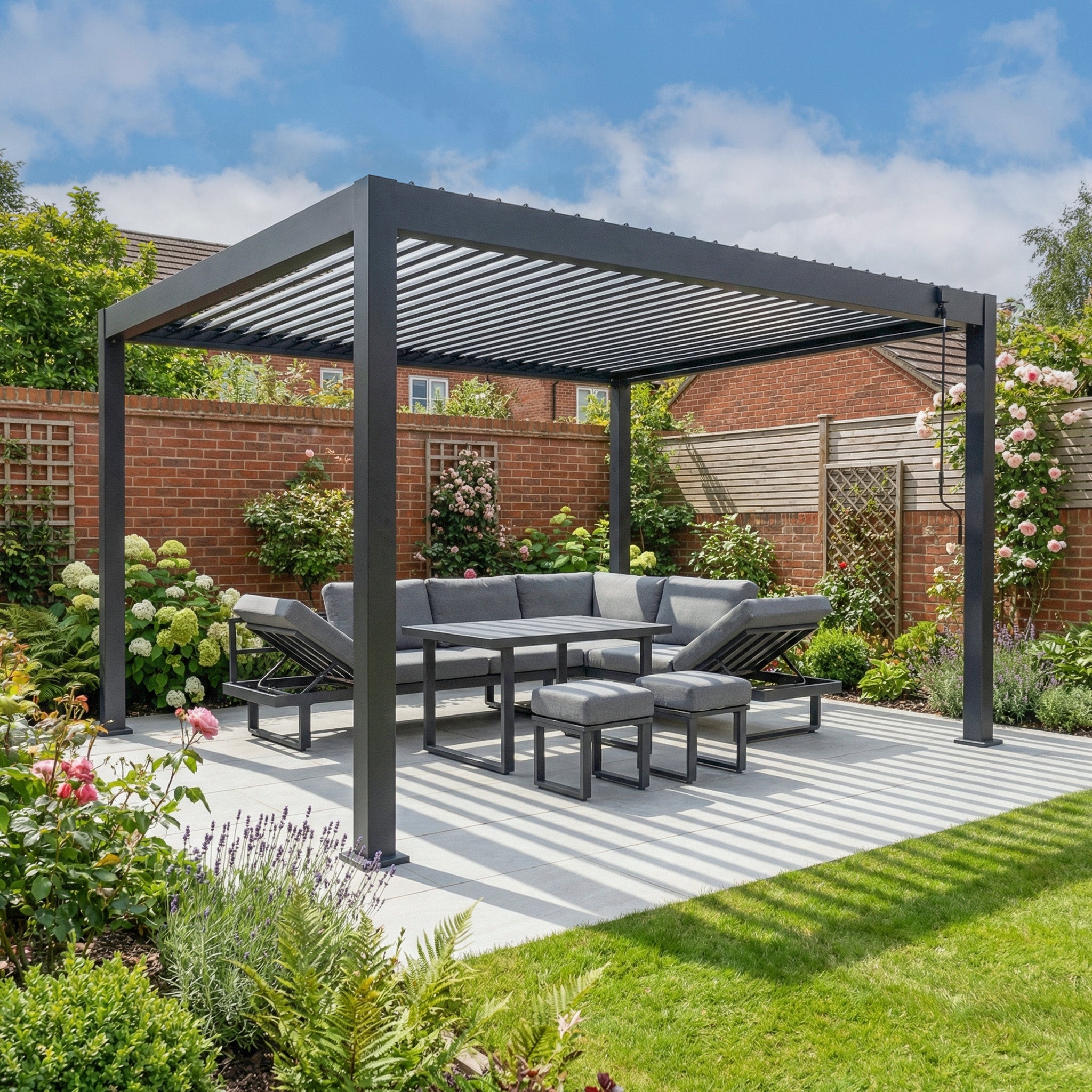 The PergoSTET Lite 3m x 4m Metal Rectangular Pergola in Grey features tilting louvres and pairs perfectly with gray outdoor seating on a patio, set amid a lush, blooming garden.