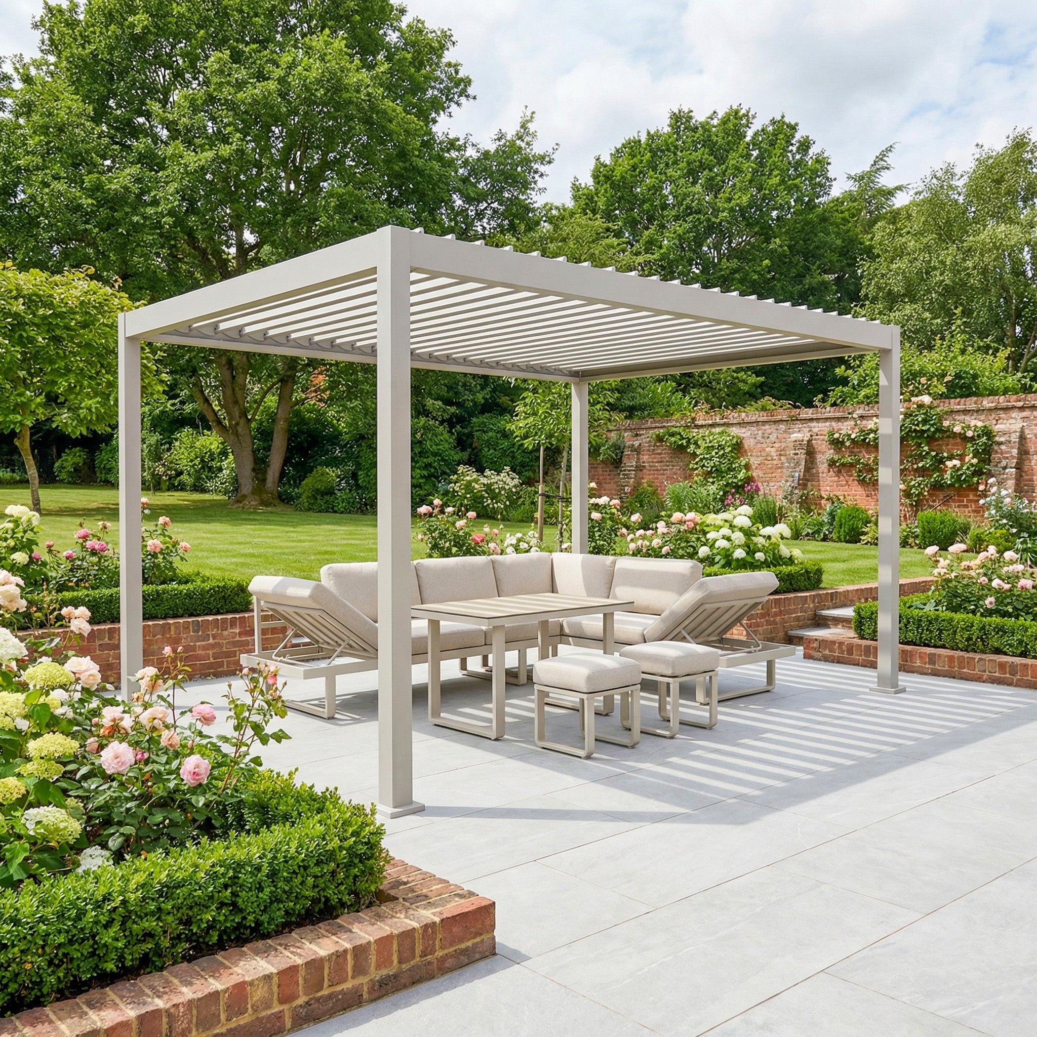 The PergoSTET Lite 3m x 4m Metal Rectangular Pergola in Latte provides outdoor shade with tilting louvres and features cozy cushioned seating, set within a landscaped garden filled with flowers and greenery.