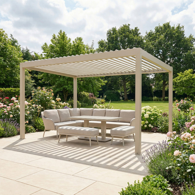 The PergoSTET Plus Frame Only 3m x 4m Rectangular Pergola with LED Lighting in Latte is set on a patio with a cushioned sectional, table, and surrounded by flowering garden plants.