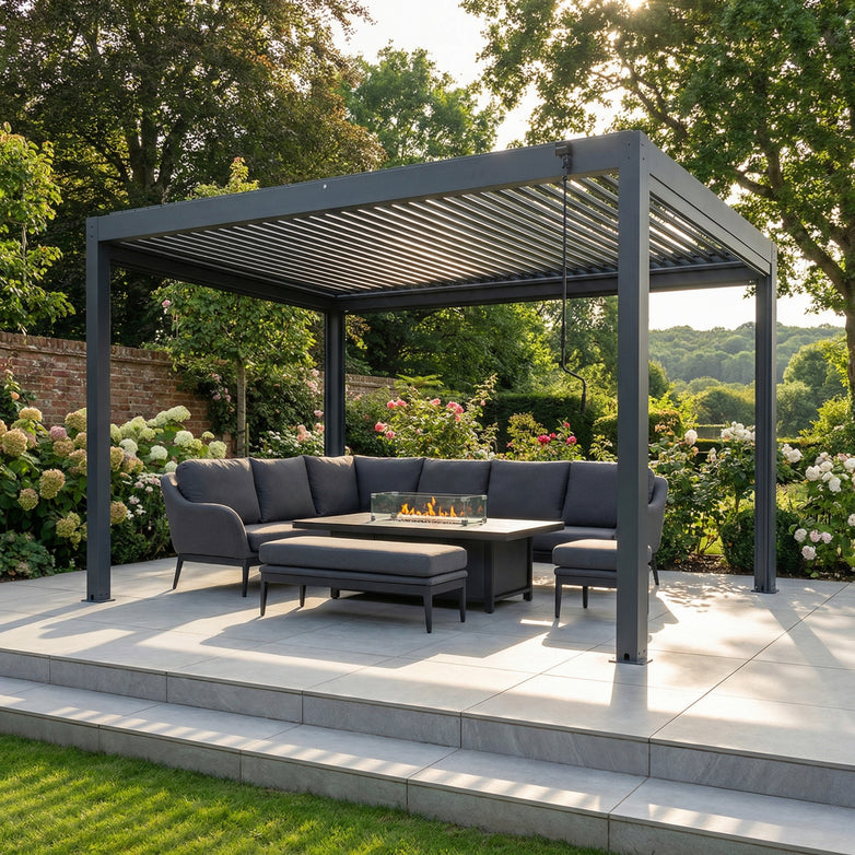 Modern outdoor patio with the PergoSTET Plus 3m x 4m Grey Rectangular Pergola frame featuring LED lighting, a sectional sofa, and fire pit table, all set amidst lush greenery.