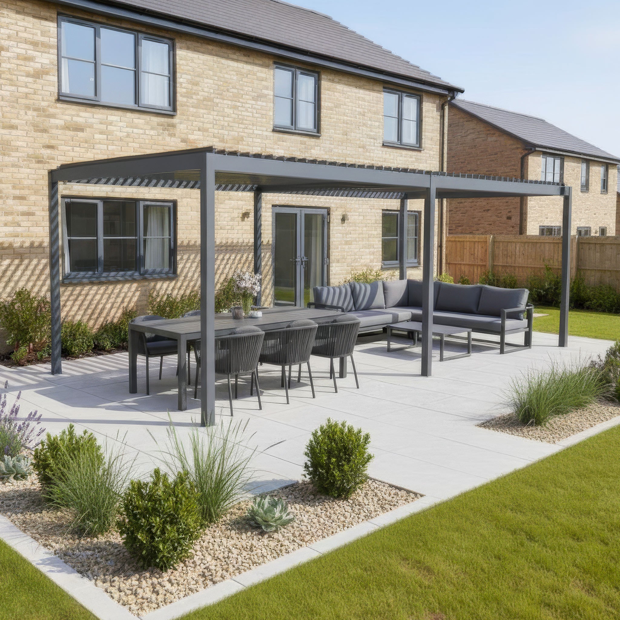 A modern patio features the PergoSTET Lite Neo 3m x 6m Metal Rectangular Pergola in Grey, with a louvred roof and aluminium frame, plus dining table and sofas in the landscaped backyard of a brick house.