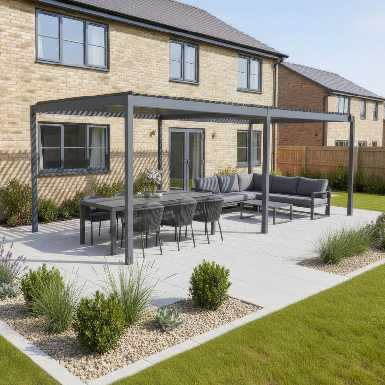 A modern patio features the PergoSTET Lite Neo 3m x 6m Metal Rectangular Pergola in Grey, with a louvred roof and aluminium frame, plus dining table and sofas in the landscaped backyard of a brick house.