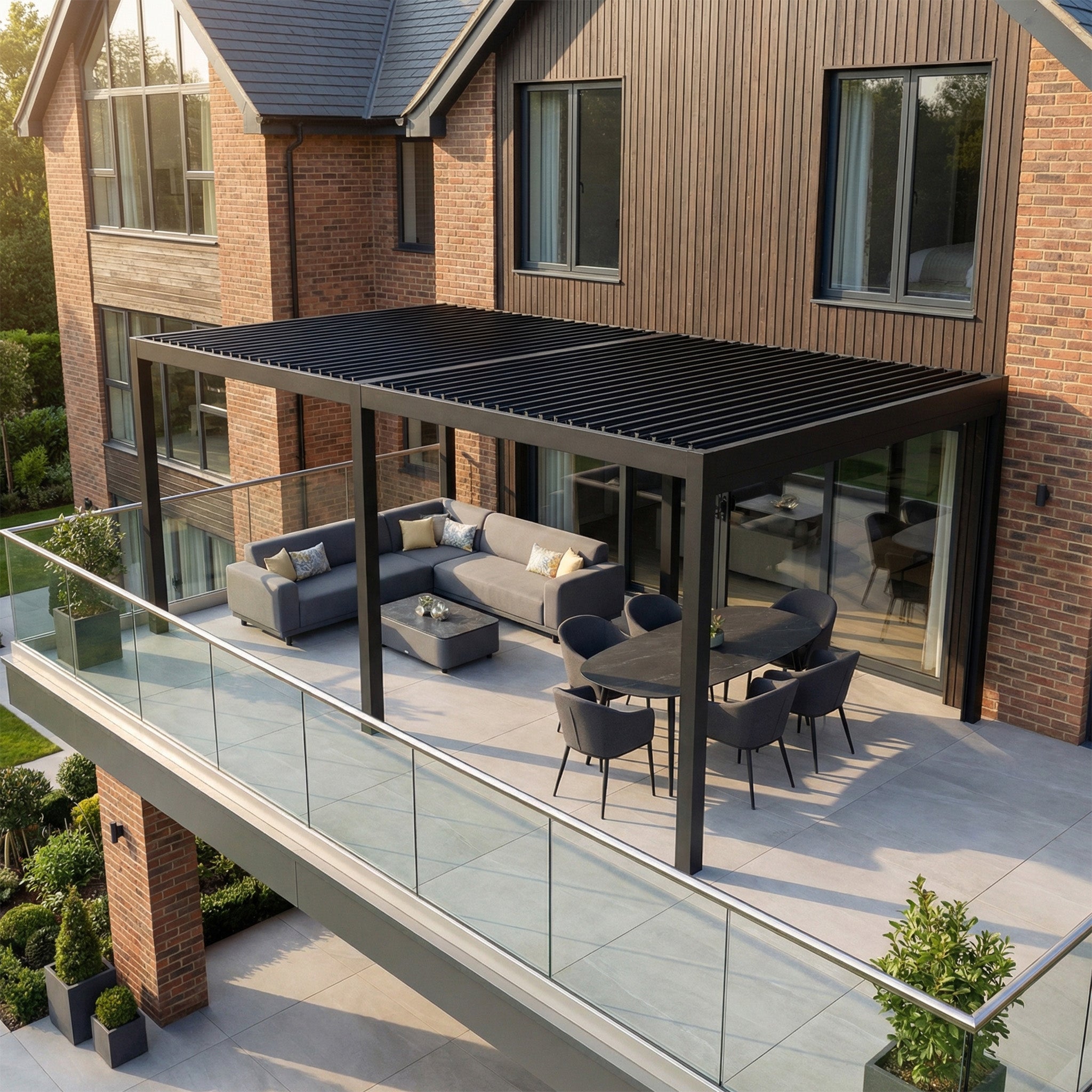 Modern patio with gray outdoor furniture and dining set under a PergoSTET Pro 3m x 6m rectangular pergola in grey with LED lighting, featuring sleek aluminium louvres and attached to a brick house.