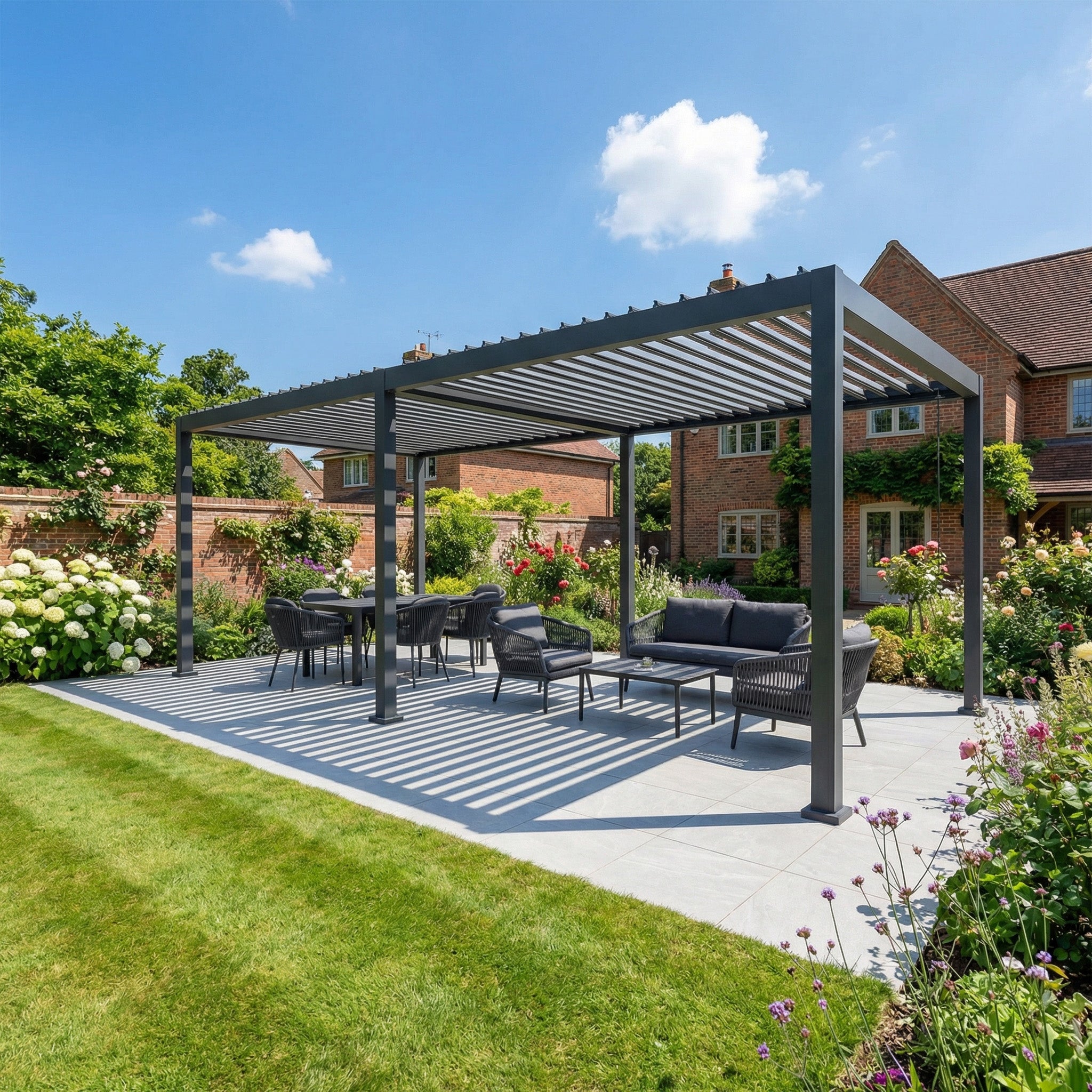 The PergoSTET Lite Neo 3m x 7m Metal Rectangular Pergola in Grey offers weather protection for an inviting outdoor seating and dining area beside a brick house, perfect for enjoying your garden under blue skies.