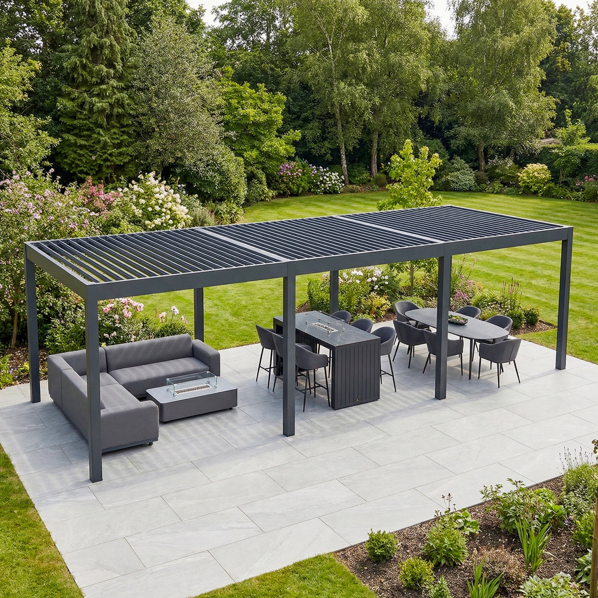 A landscaped garden features the PergoSTET Deluxe 3m x 9m Rectangular Pergola with motorised LED louvres in grey, creating a modern outdoor seating and dining area surrounded by lush greenery.