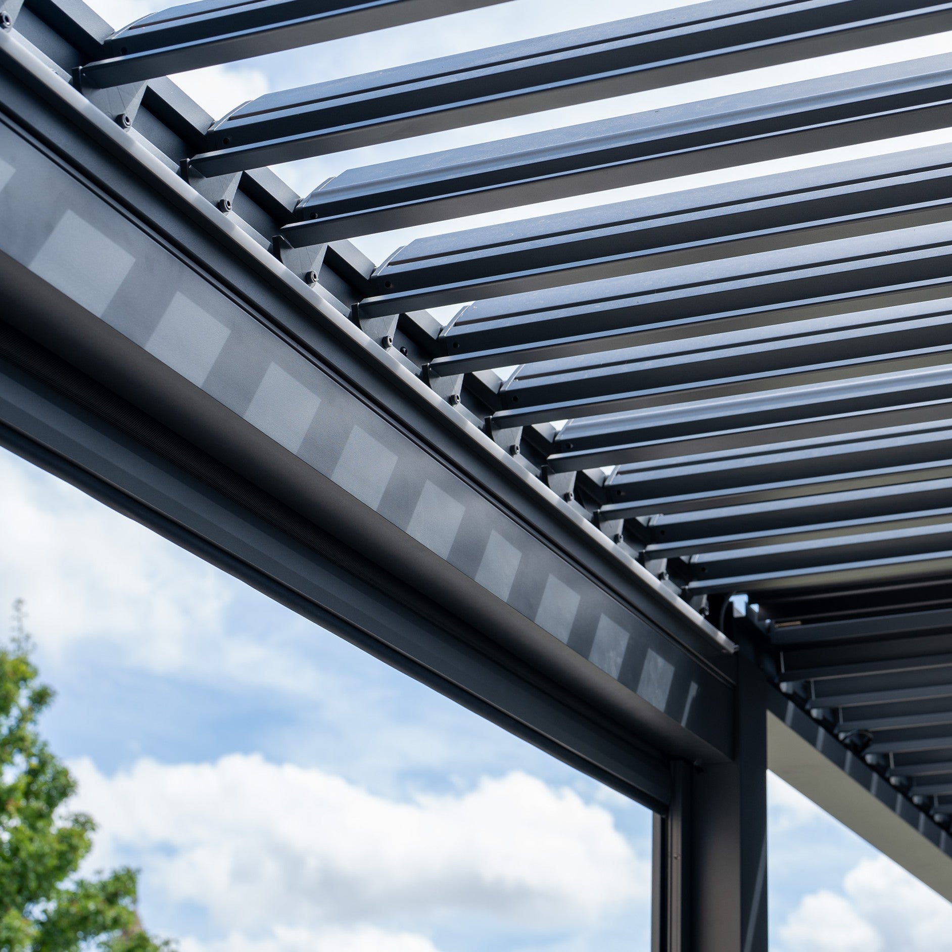 Close-up of the PergoSTET Deluxe 3m x 6m Rectangular Pergola, showcasing its sleek metal beams and motorised LED louvres against a cloudy blue sky.