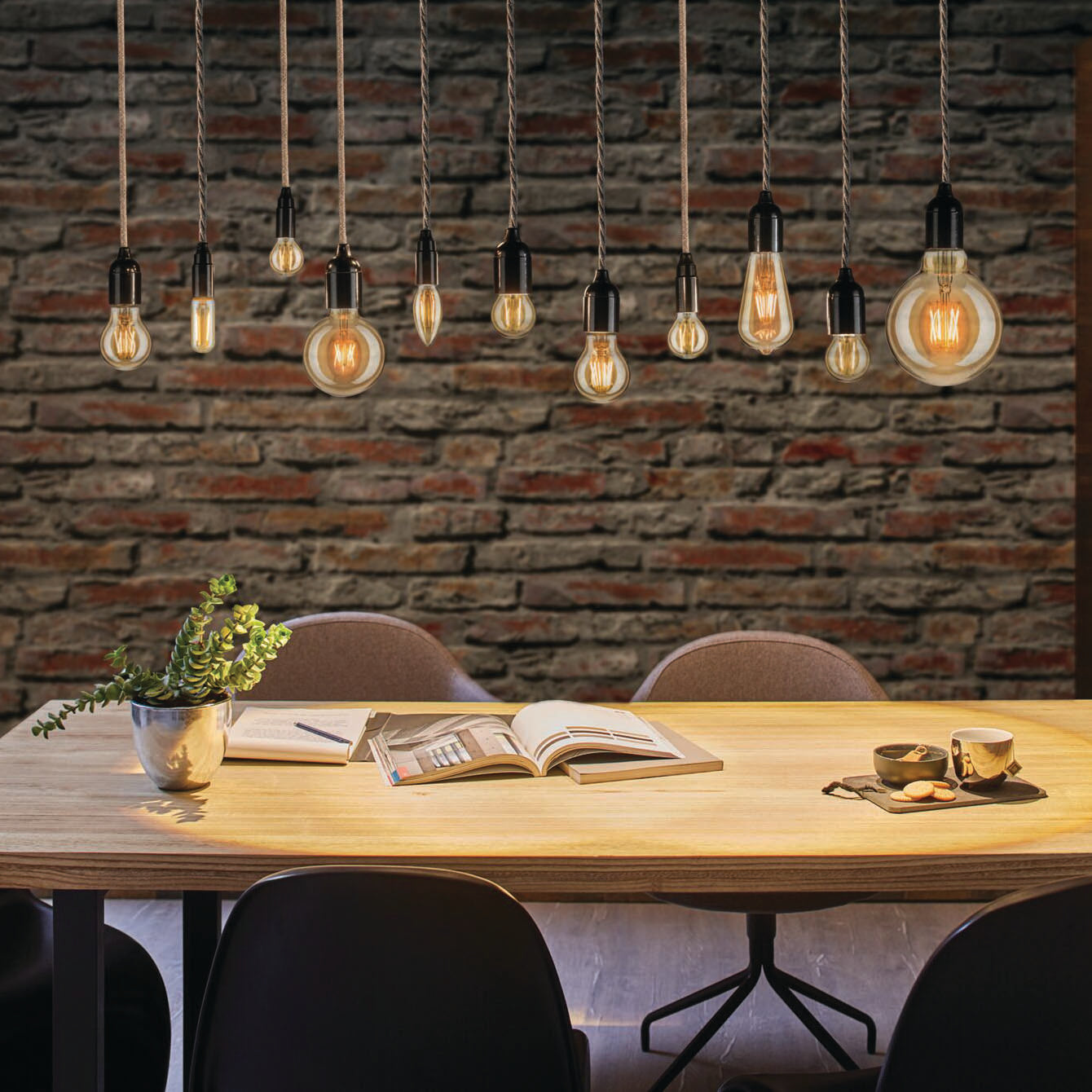 Paulmann's Filament LED Candle Bulb 2W E14 casts a warm glow over the wooden table adorned with books, coffee cups, and a potted plant against a rustic brick wall, seamlessly blending energy-efficient LED technology with vintage charm.