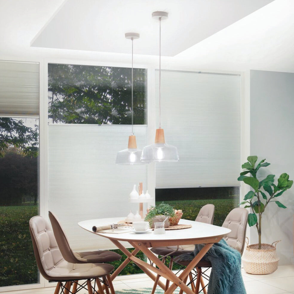 Modern dining area featuring a round table, four chairs, and pendant lights casting a warm white glow from Paulmann's Filament LED Pear Bulbs. Large windows with blinds enhance the inviting atmosphere.