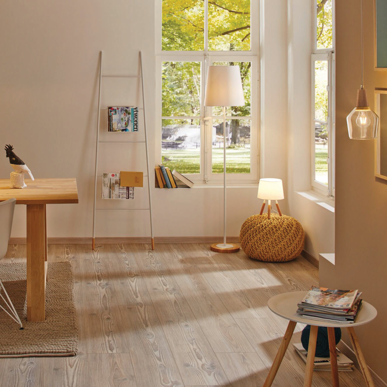 A cozy room featuring large windows, a wooden table, and a ladder bookshelf is illuminated by the inviting warm white glow of the Paulmann Filament LED Pear Bulb 5W E27.