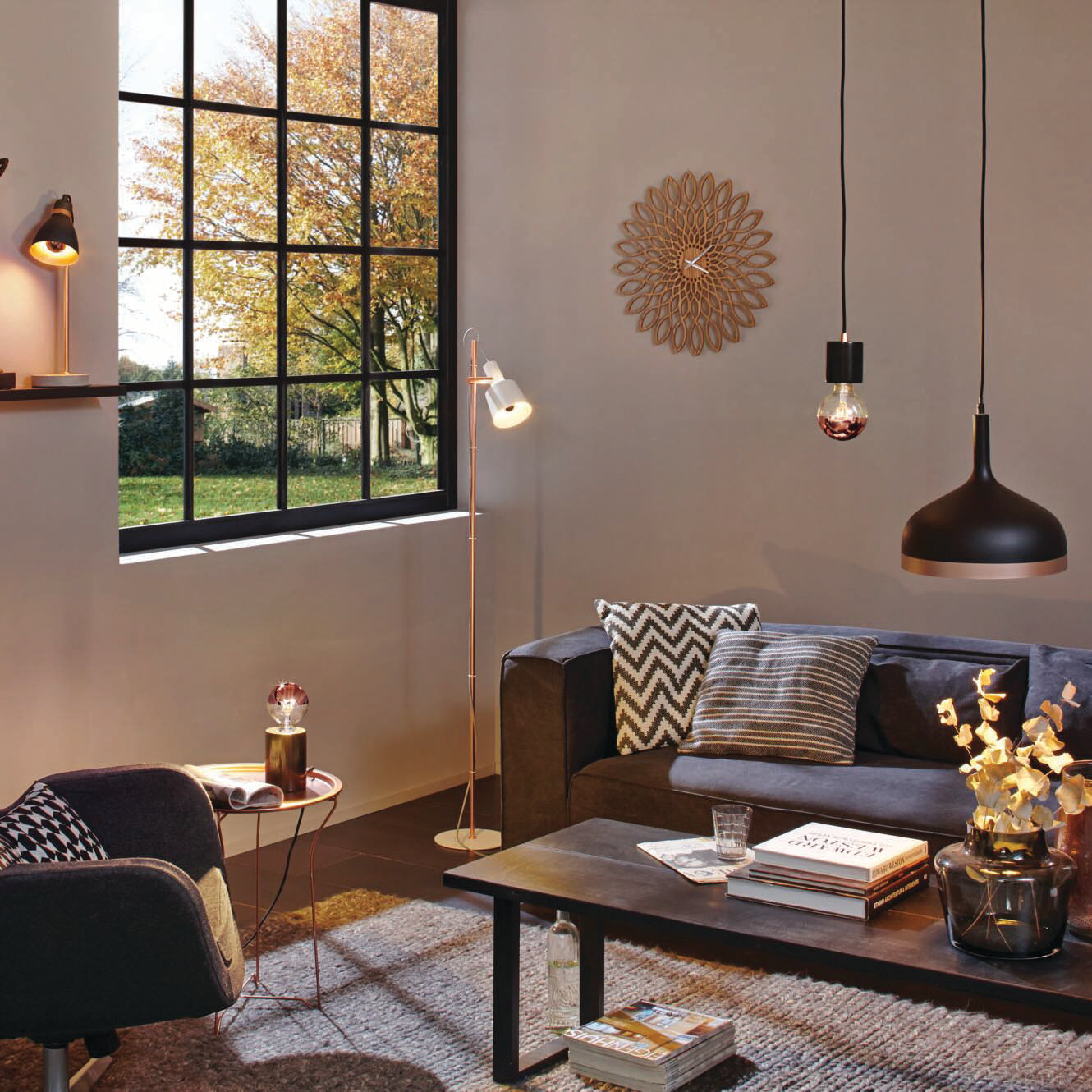 A cozy living room with modern decor, a large window, and black pendant lights. The fall foliage outside enhances the inviting atmosphere, beautifully paired with the warm white light from the Paulmann Standard LED Drop Crown Mirror Bulb 2.6W E14 Silver.