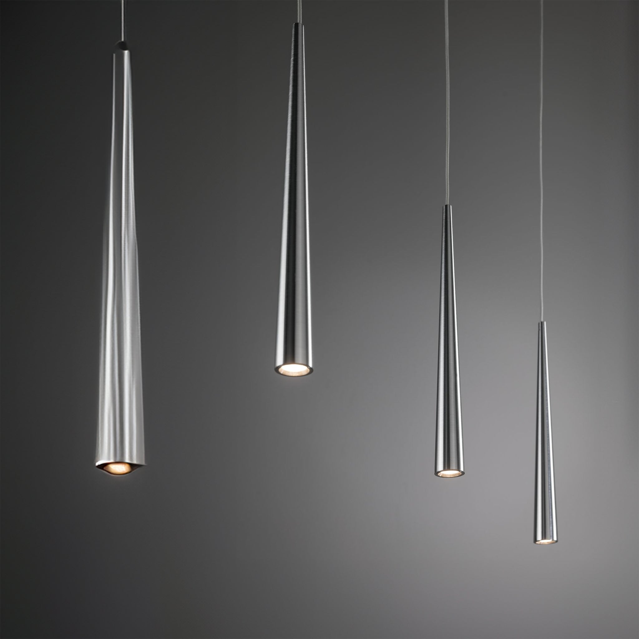 Four modern Gutta 23W LED dimmable pendant lights by Paulmann, with a brushed aluminum finish, elegantly hang at varying lengths against a gray background, each featuring an adjustable cable for customized height.