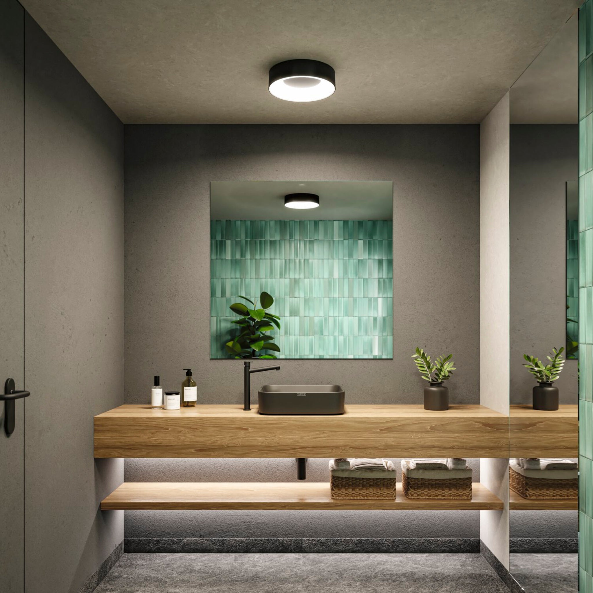A modern bathroom featuring a green tiled wall, wooden vanity, and plants is enhanced by the soothing lighting effect of a ceiling luminaire. The square mirror reflects the glow from the Paulmann - Casca 18W LED Switch 1500lm Ceiling Light in Black Matt, adding warmth and ambiance to the space.