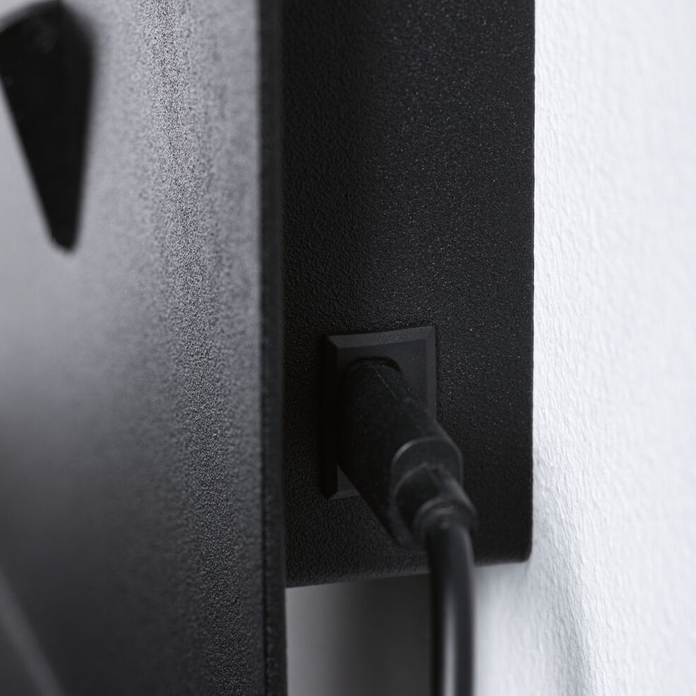 Close-up of the USB charging port cable from the Paulmann - Malena 5W Wall Light in Black Matt, connected at the back of a flat-screen TV mounted on a wall.