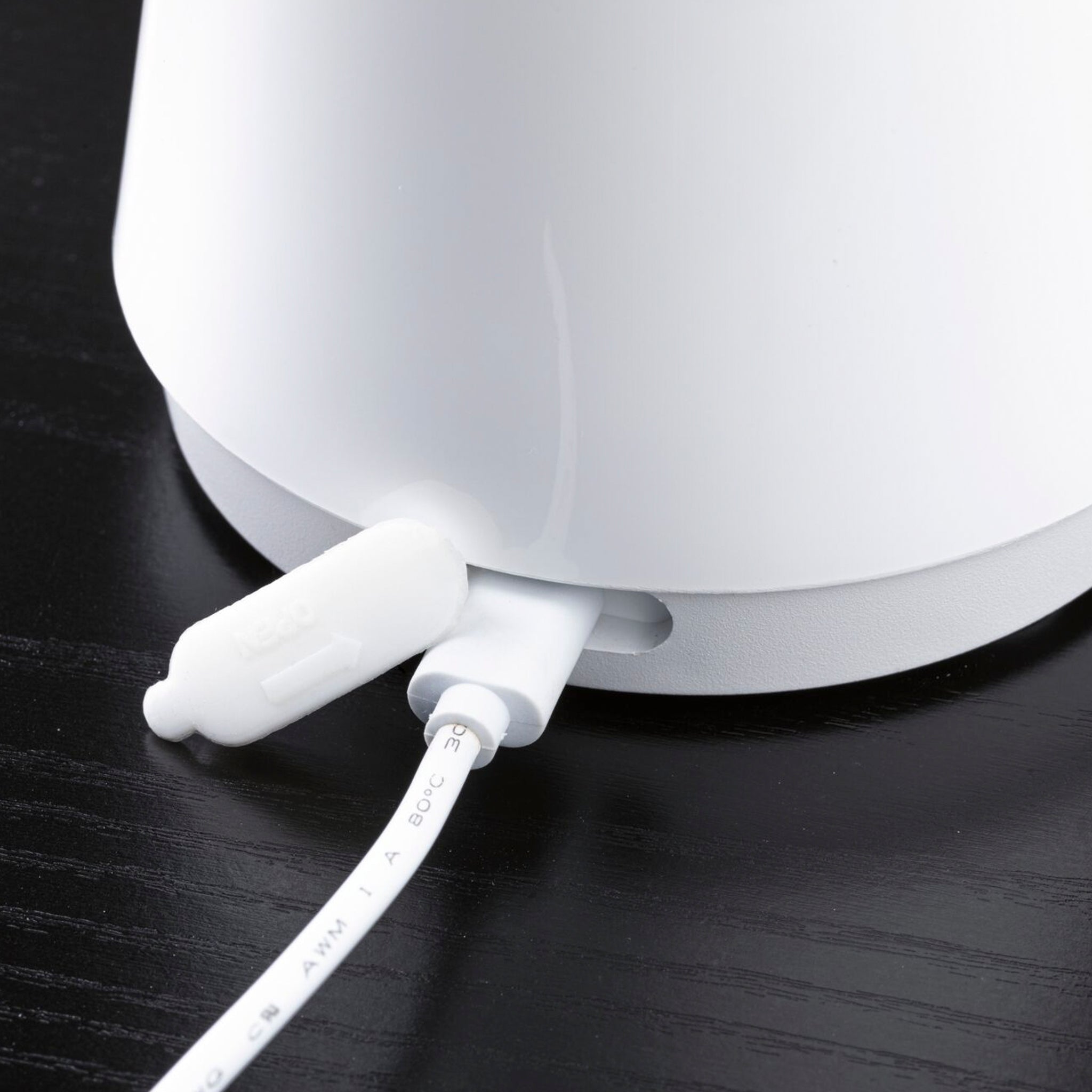 Close-up of a white USB-C cable plugged into the Paulmann - Onzo 2.6W LED Mobile Table Lamp with 3-Step Dim in White on a dark surface.