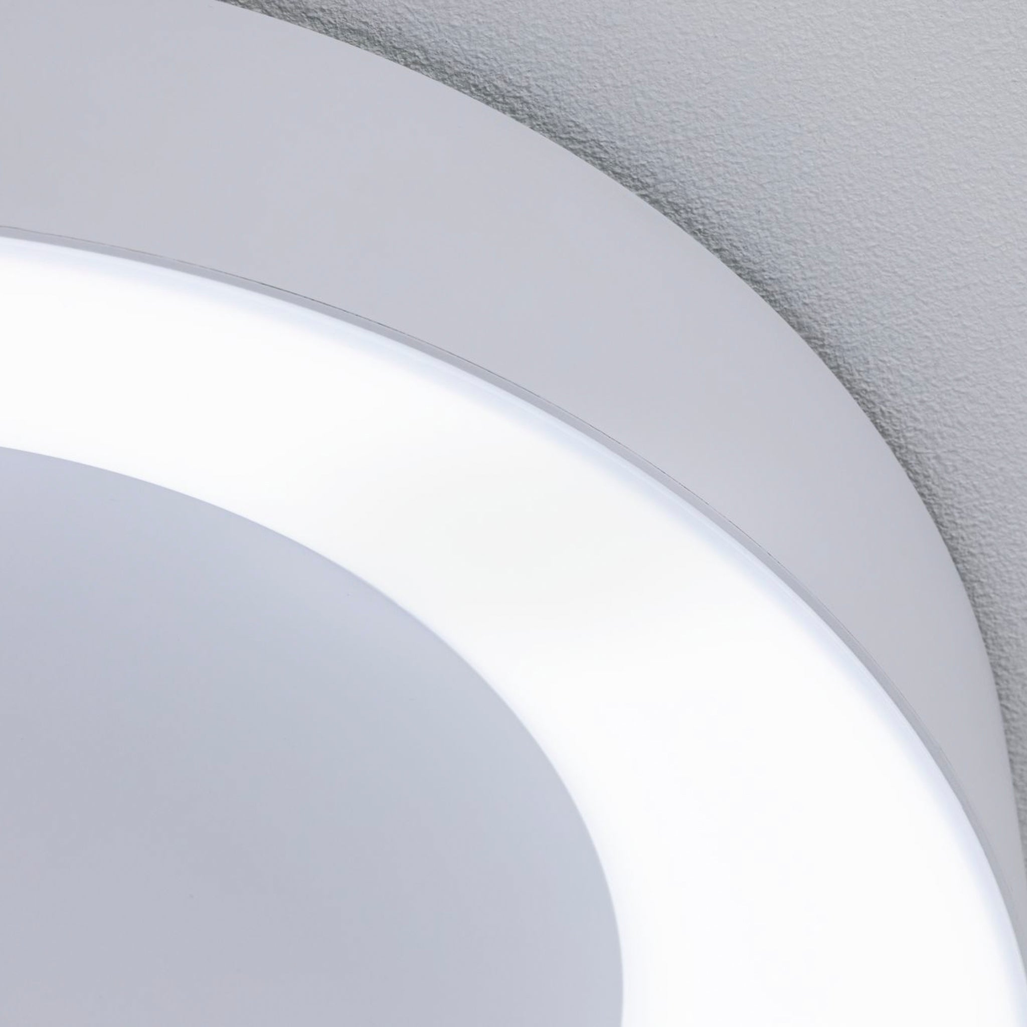 Close-up of the Paulmann - Casca 25W LED Switch 2100lm Ceiling Light in white, mounted on a textured gray ceiling, showcasing its smooth and sleek design with subtle light color adjustment for an elegant lighting effect.