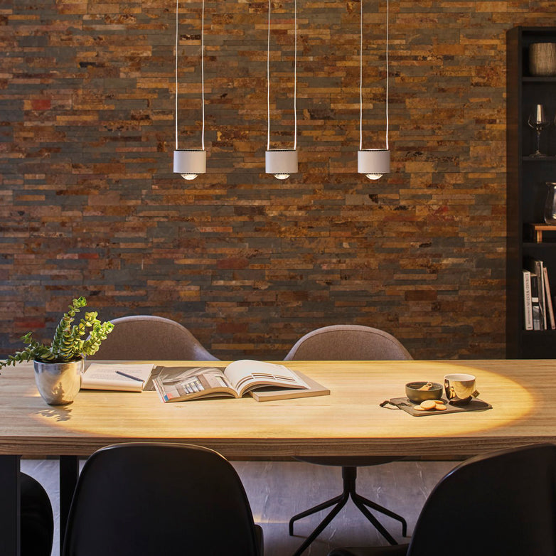 Intimate dining space enhanced by a sophisticated touch with the Paulmann - Aldan 28W LED Dimmable 3 Lamp Pendant Light in Brushed Aluminium casting a cozy radiance over the wooden table, complemented by an open book, a plant, and cups that contribute to the welcoming atmosphere.
