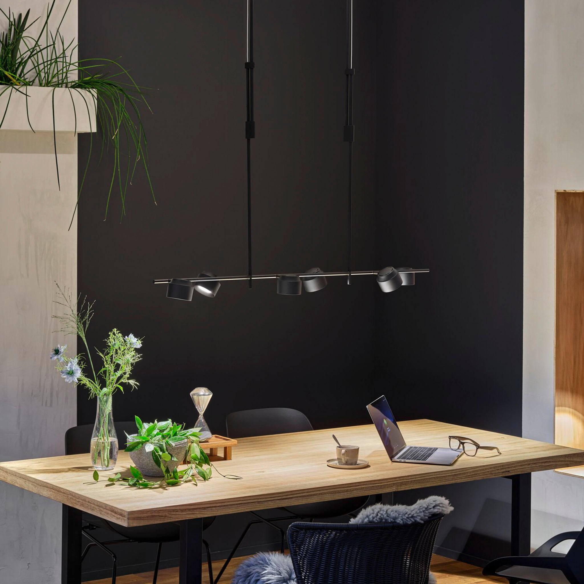 Contemporary workspace featuring a wooden table, laptop, vase with flowers, glasses, and the Paulmann Puric Pane 6.5W LED 6 Lamp Pendant Light in black, offering versatile dimming options.