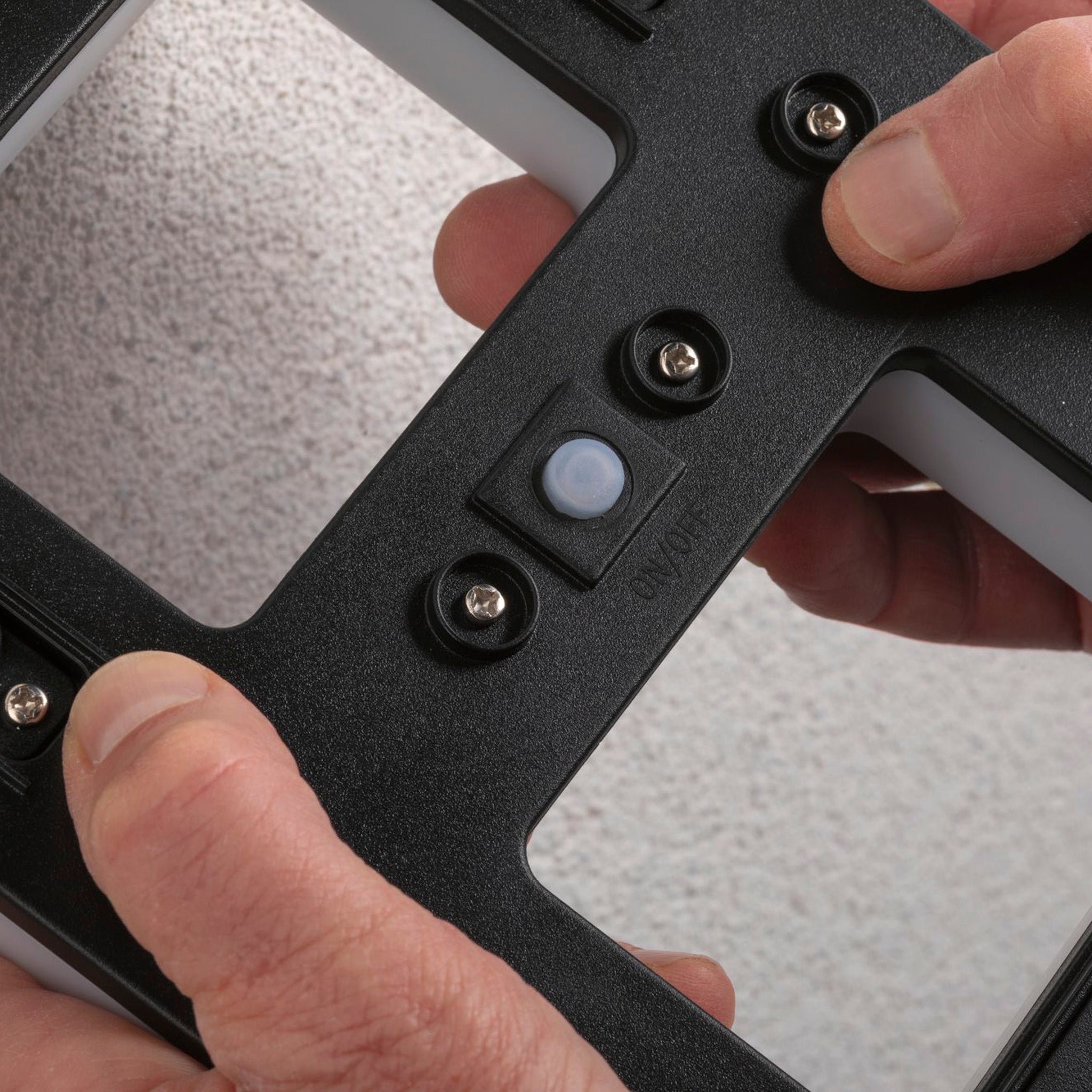 Hands adjusting a black mounting bracket with screws and a Paulmann Outdoor Solar House Number 1 LED 0.2W luminaire with a replaceable battery on a textured wall, ideal for an illuminated house number display.