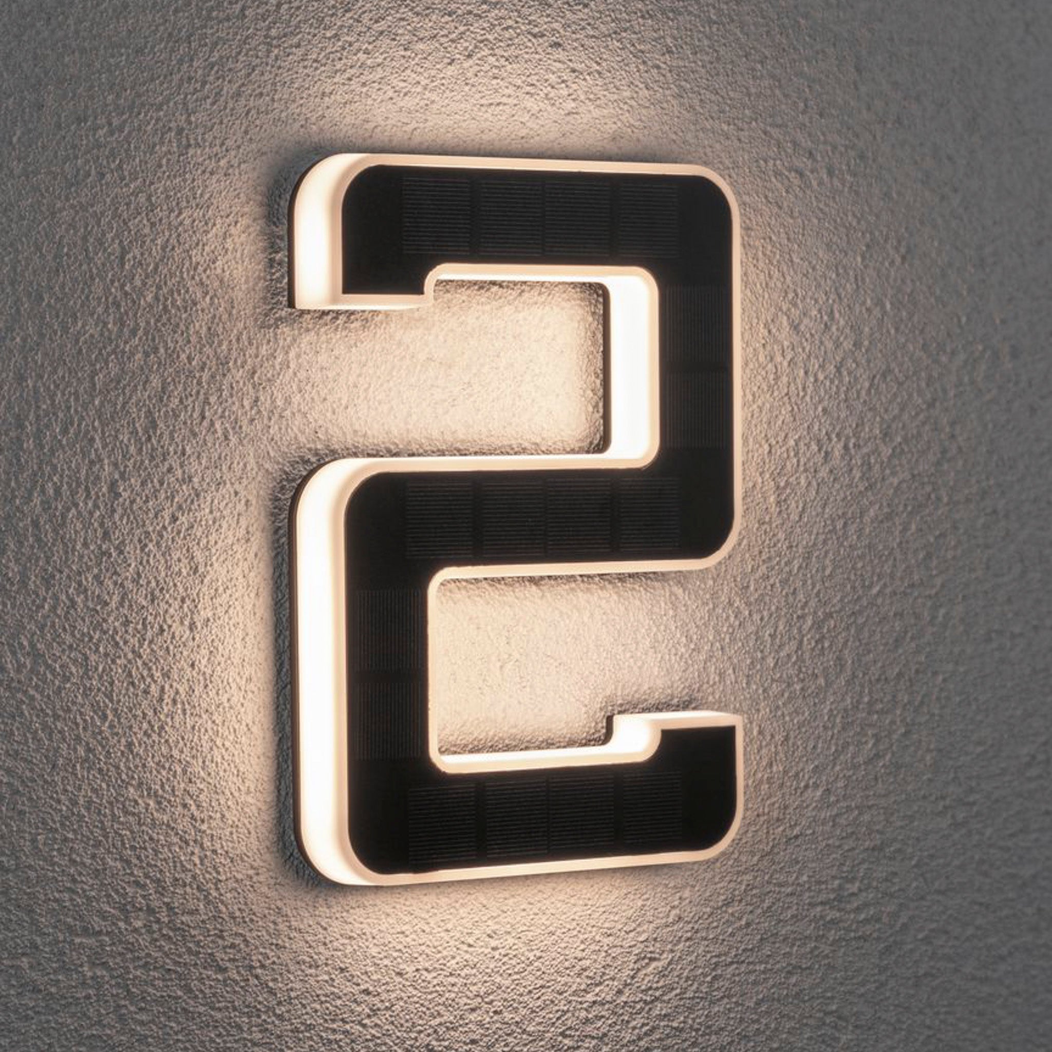 The Paulmann Outdoor Solar House Number "2" LED 0.2W, featuring a replaceable battery in black, softly glows with solar-powered backlighting on a textured wall.