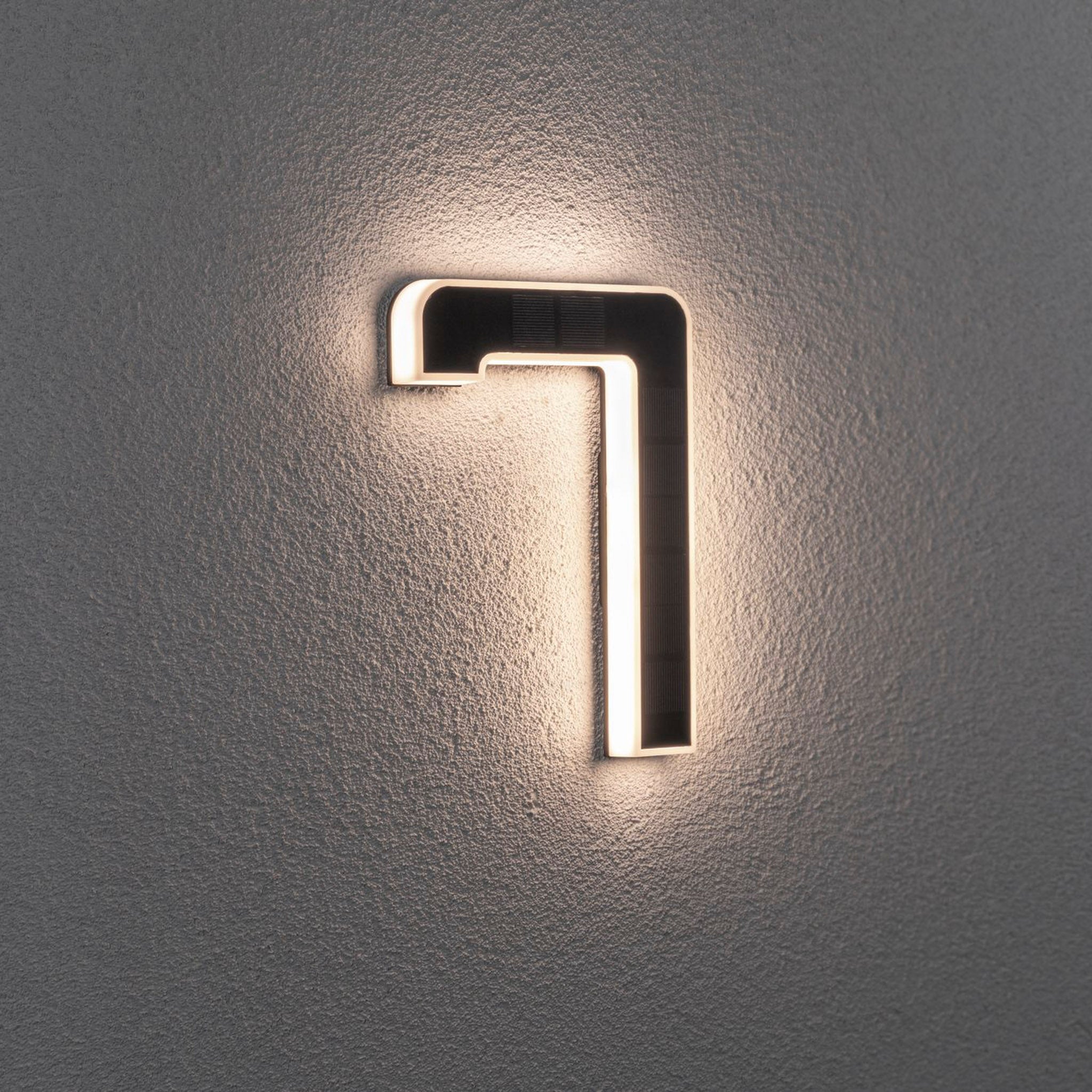 The Paulmann Outdoor Solar House Number 7 LED glows softly on a textured wall, featuring a 0.2W light and replaceable battery in black.