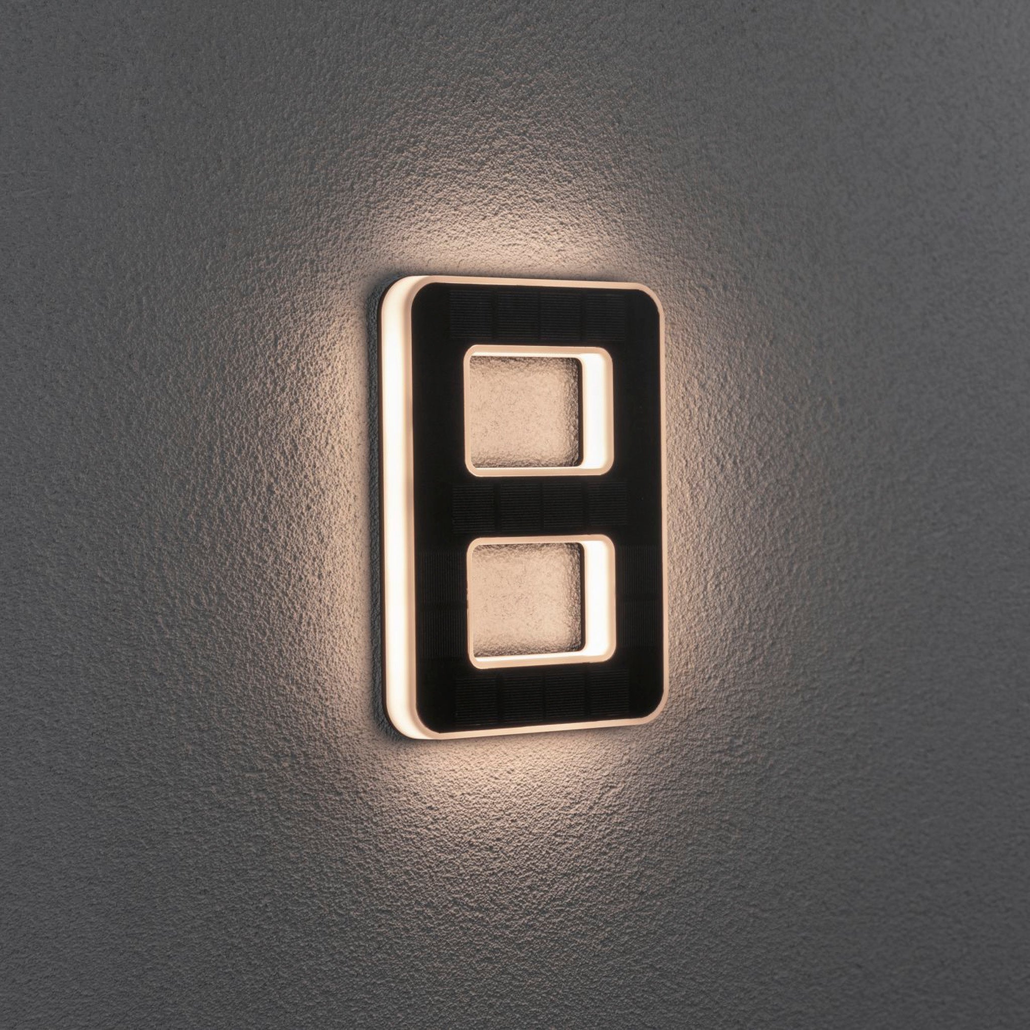 The Paulmann Outdoor Solar House Number 8 LED, with a replaceable battery in black, softly illuminates against a gray wall, serving as an elegant lighting solution for displaying house numbers.