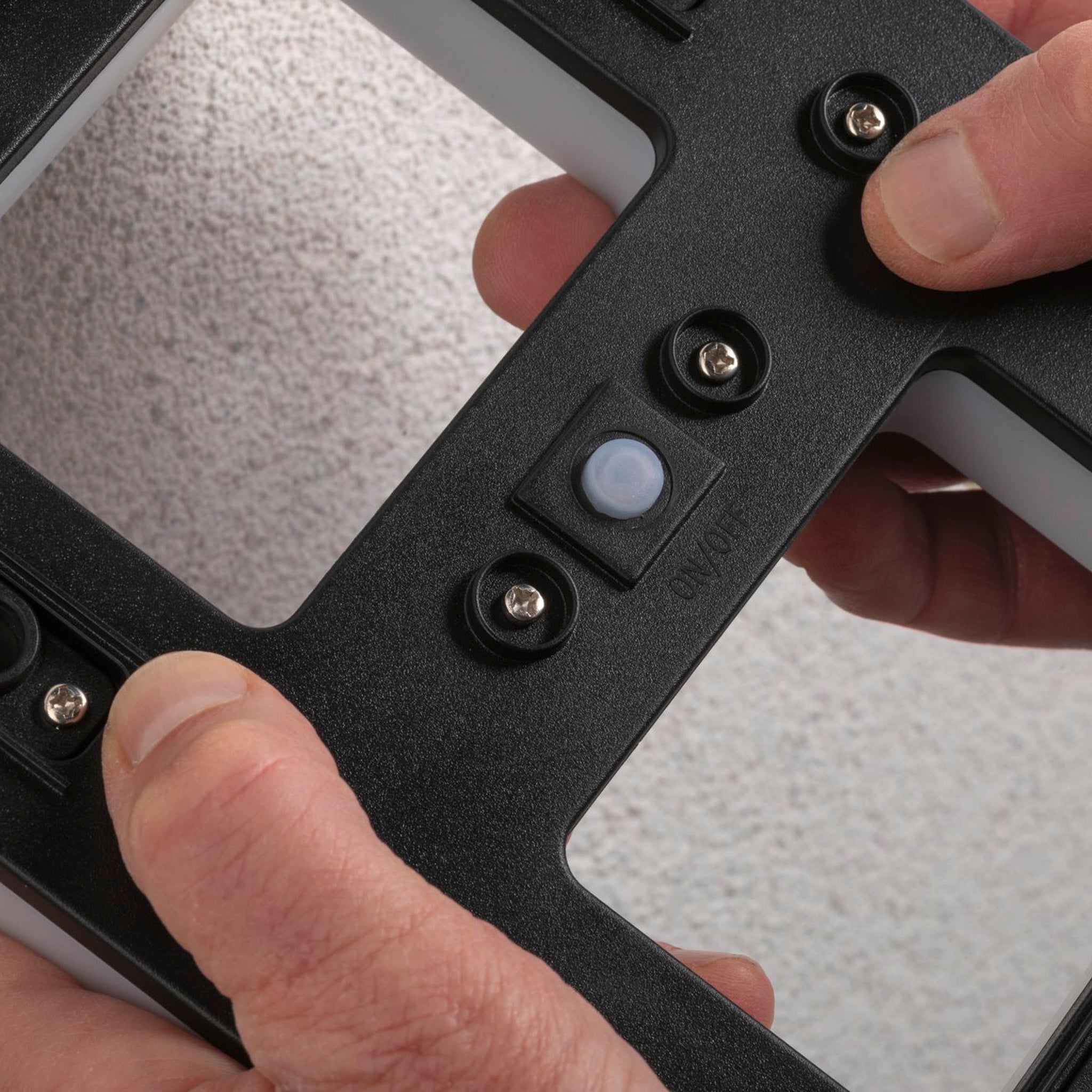 Hands adjusting the Paulmann Outdoor Solar House Number 9 LED 0.2W with a replaceable battery in black on a textured wall, preparing for installation.