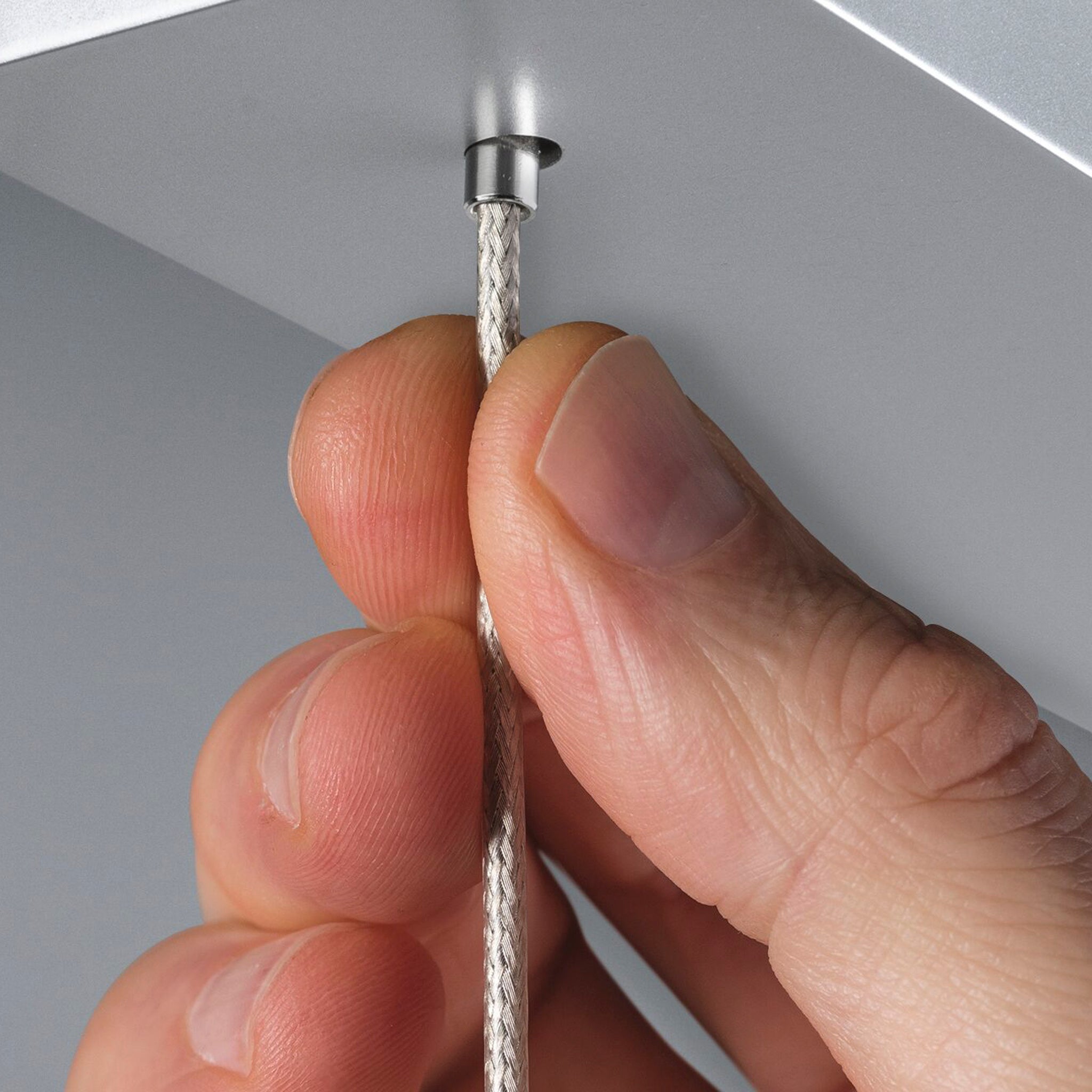 Close-up of a hand threading a braided cord through a small metal opening in the light-colored, height-adjustable surface of the Paulmann - Lento 37W LED Dimmable Pendant Light in Chrome Matt.