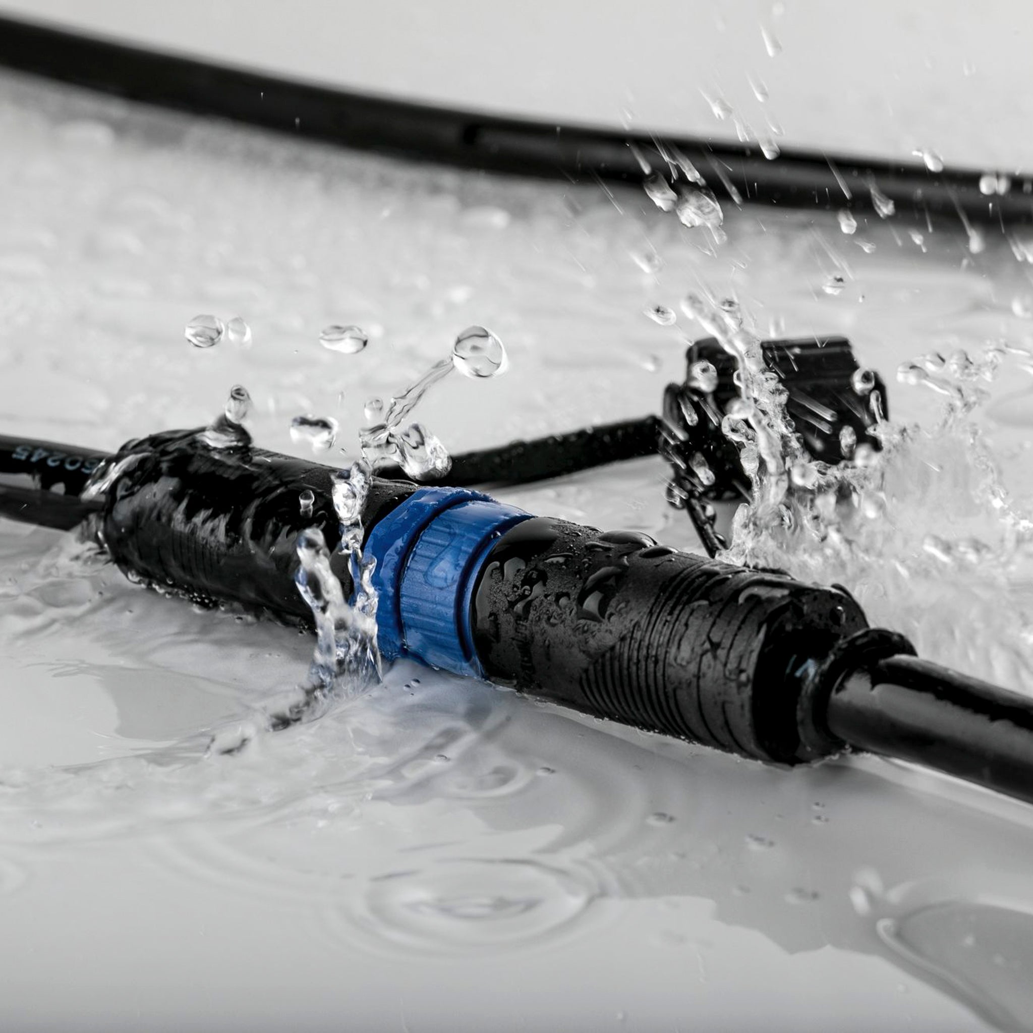 The Paulmann - Plug & Shine Outdoor 10m Cables with 2 Outputs in Black, featuring IP68 immersion protection, are submerged in splashing water on a reflective surface.