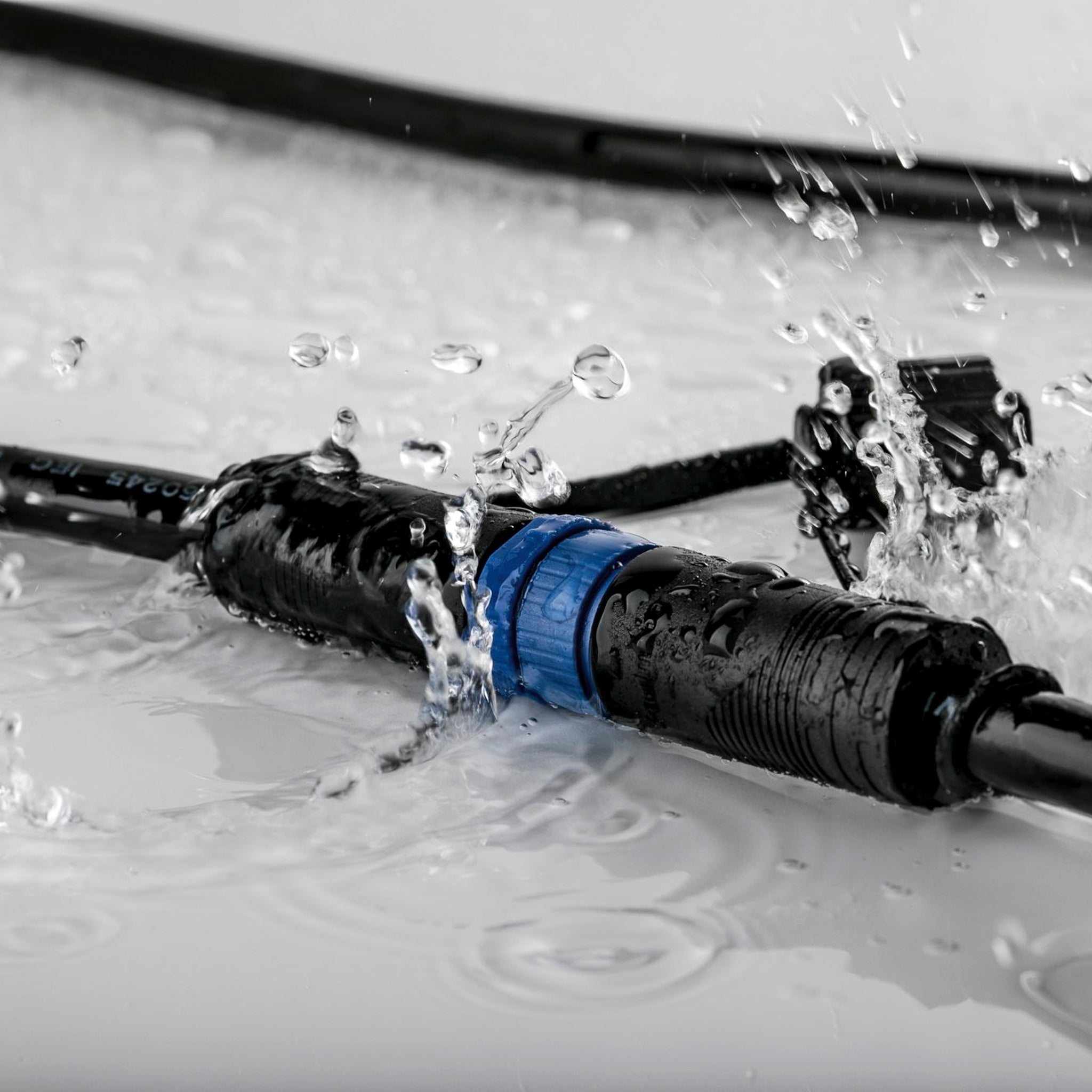 Close-up of the Paulmann - Plug & Shine Outdoor 1m Cables with 3 Outputs in Black, showcasing its IP68 immersion protection as it remains submerged in water with splashes cascading around, ensuring reliable performance in outdoor spaces.