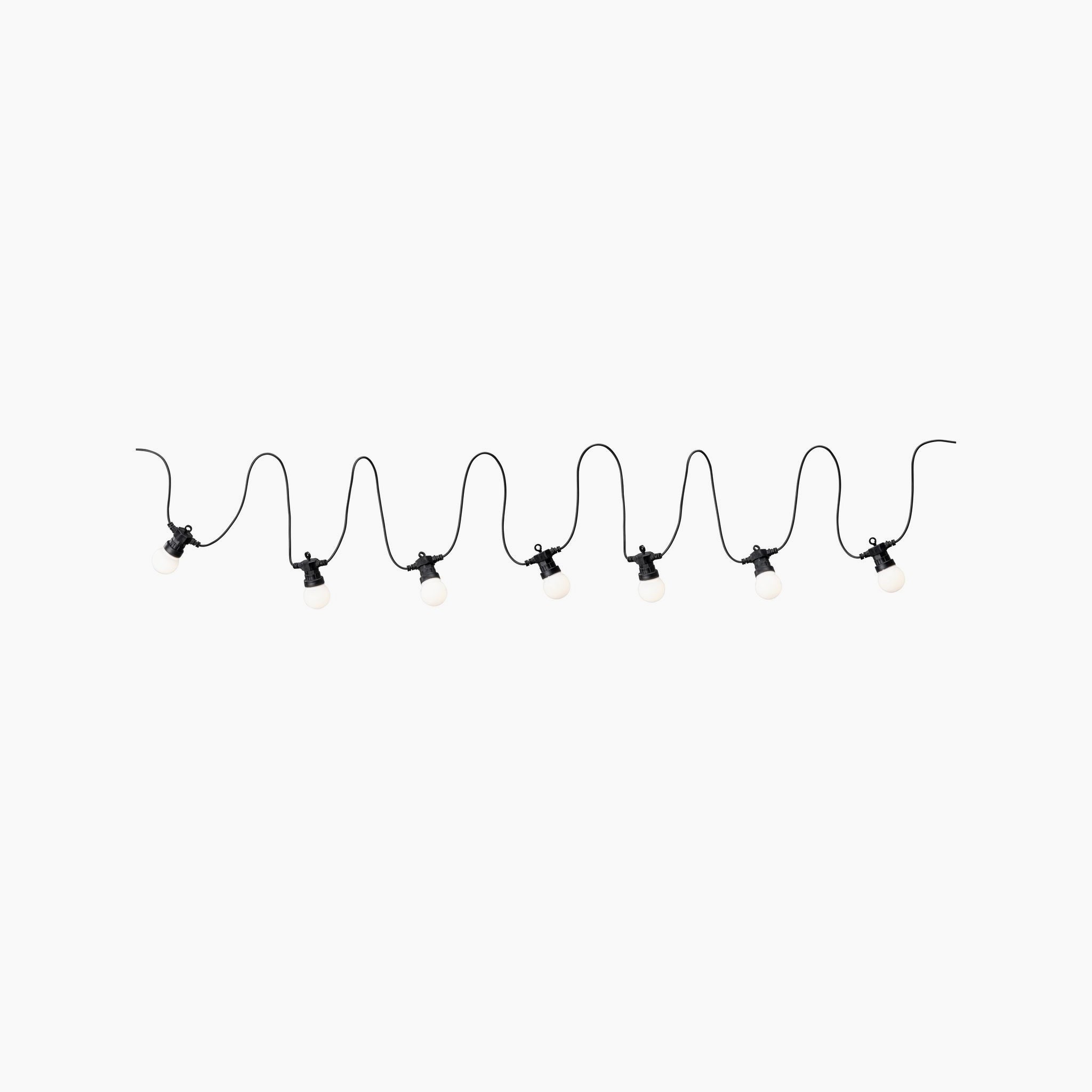 A string of warm white LED fairy lights, elegantly hanging on an anthracite wire set against a plain white background, is perfect for crafting a cozy atmosphere. This Paulmann - Plug & Shine Outdoor 1.5W lighting system adds elegance and charm to any outdoor setting.