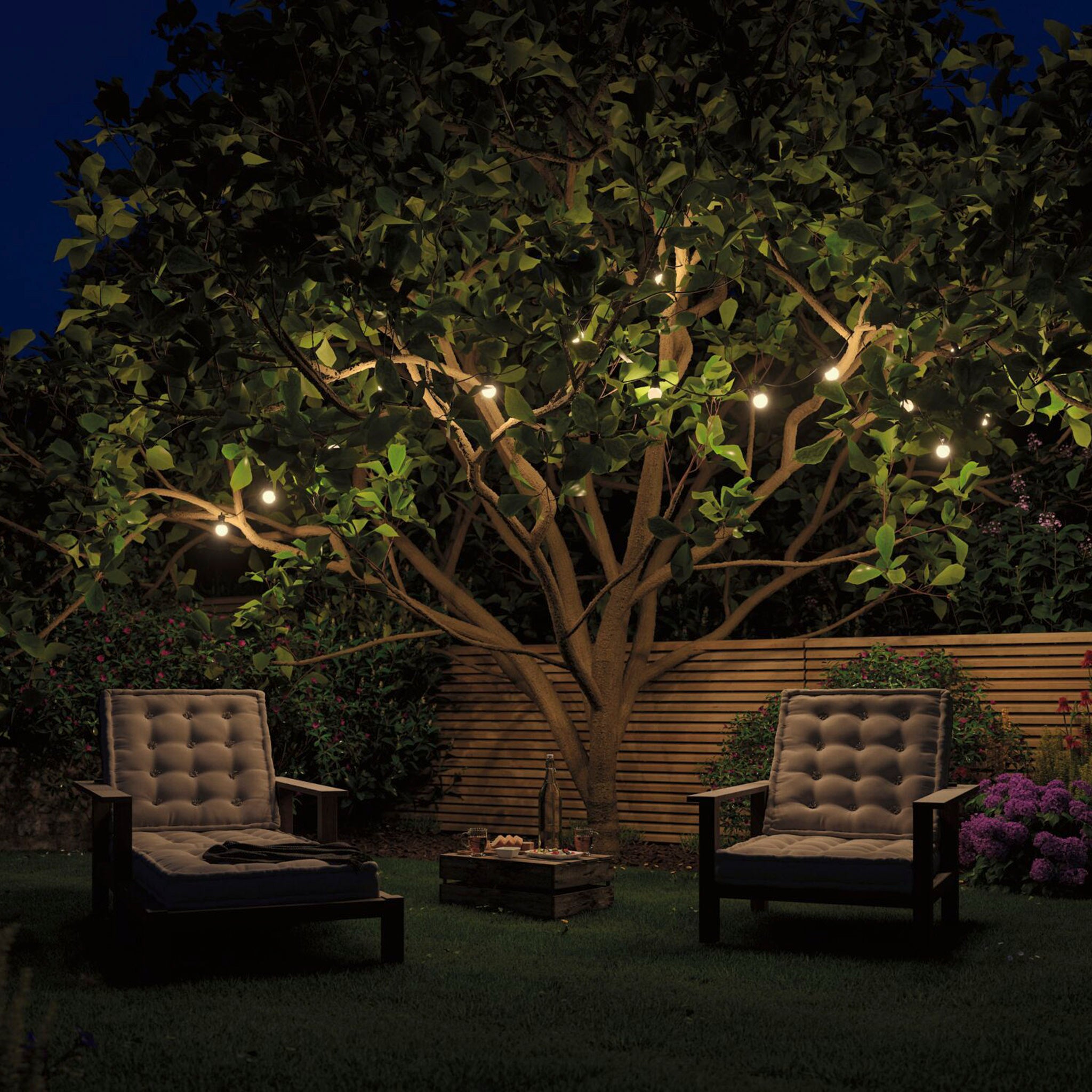 Two cushioned chairs under a tree with the warm glow of Paulmann - Plug & Shine Outdoor 1.5W LED Fairy Lights in Anthracite create a cozy outdoor setting, enhancing the charm of the lighting.