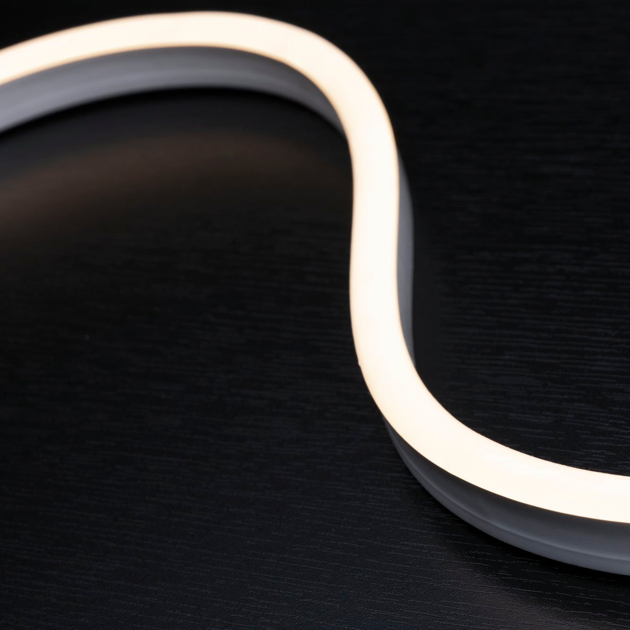 Close-up of a wavy, weather-resistant Paulmann - Plug & Shine Outdoor 31W LED Light Strip in Warm White emitting homogeneous light against a dark background.