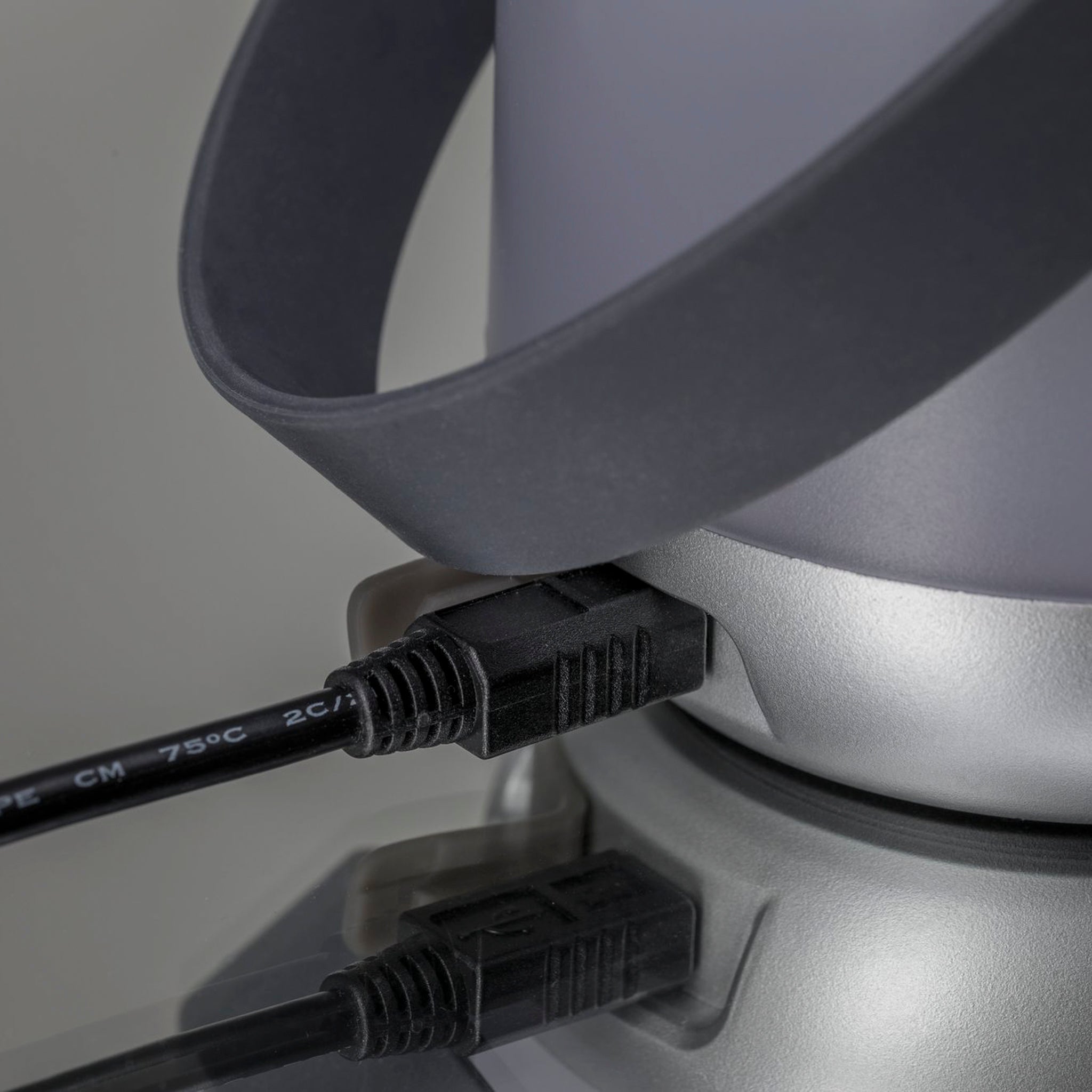 Close-up of a gray plug inserted into the elegant, silver Paulmann - Outdoor Clutch 6W LED Mobile Table Lamp on a reflective surface, casting a pleasant light.