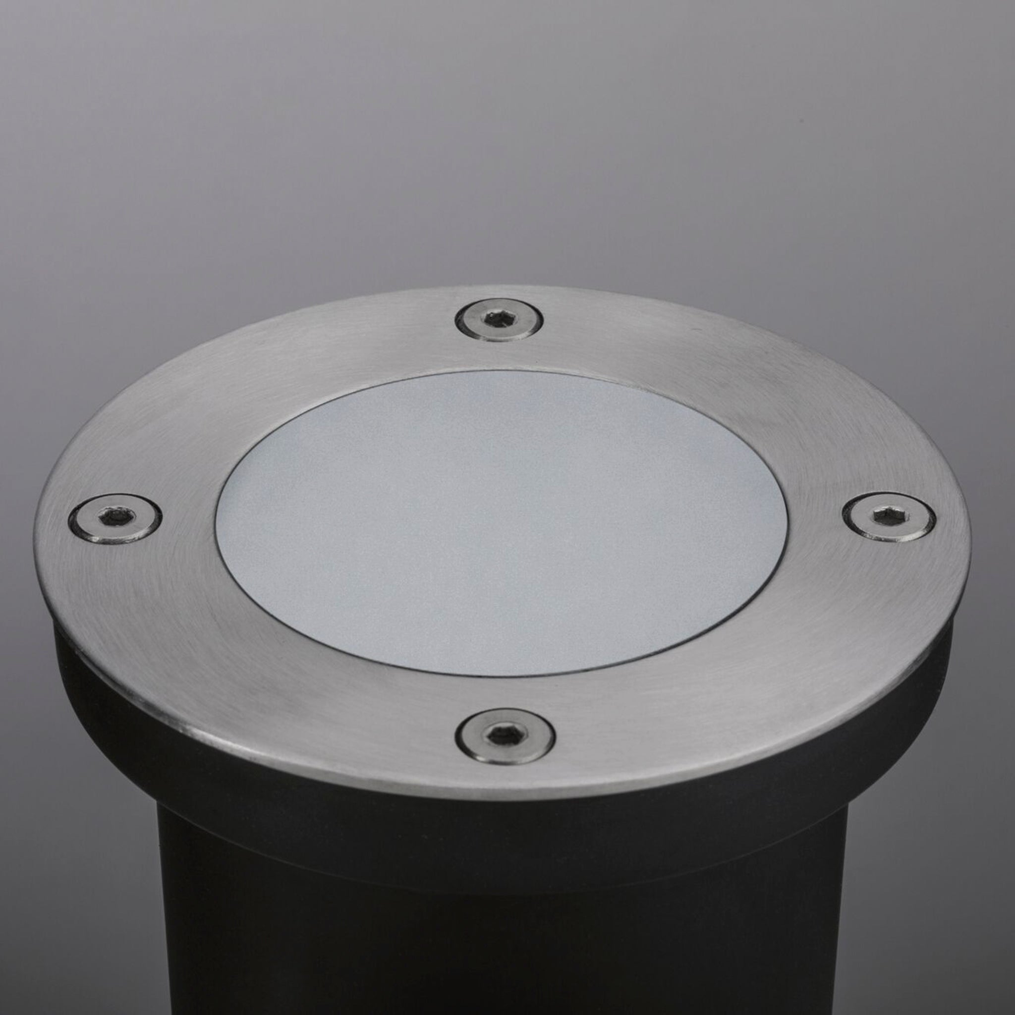 The Paulmann - Plug & Shine Outdoor 3.8W LED Recessed Floor Individual Round Spotlight in Stainless Steel, featuring a round metal design with four screws on a dark cylindrical base, is set against a gray background.