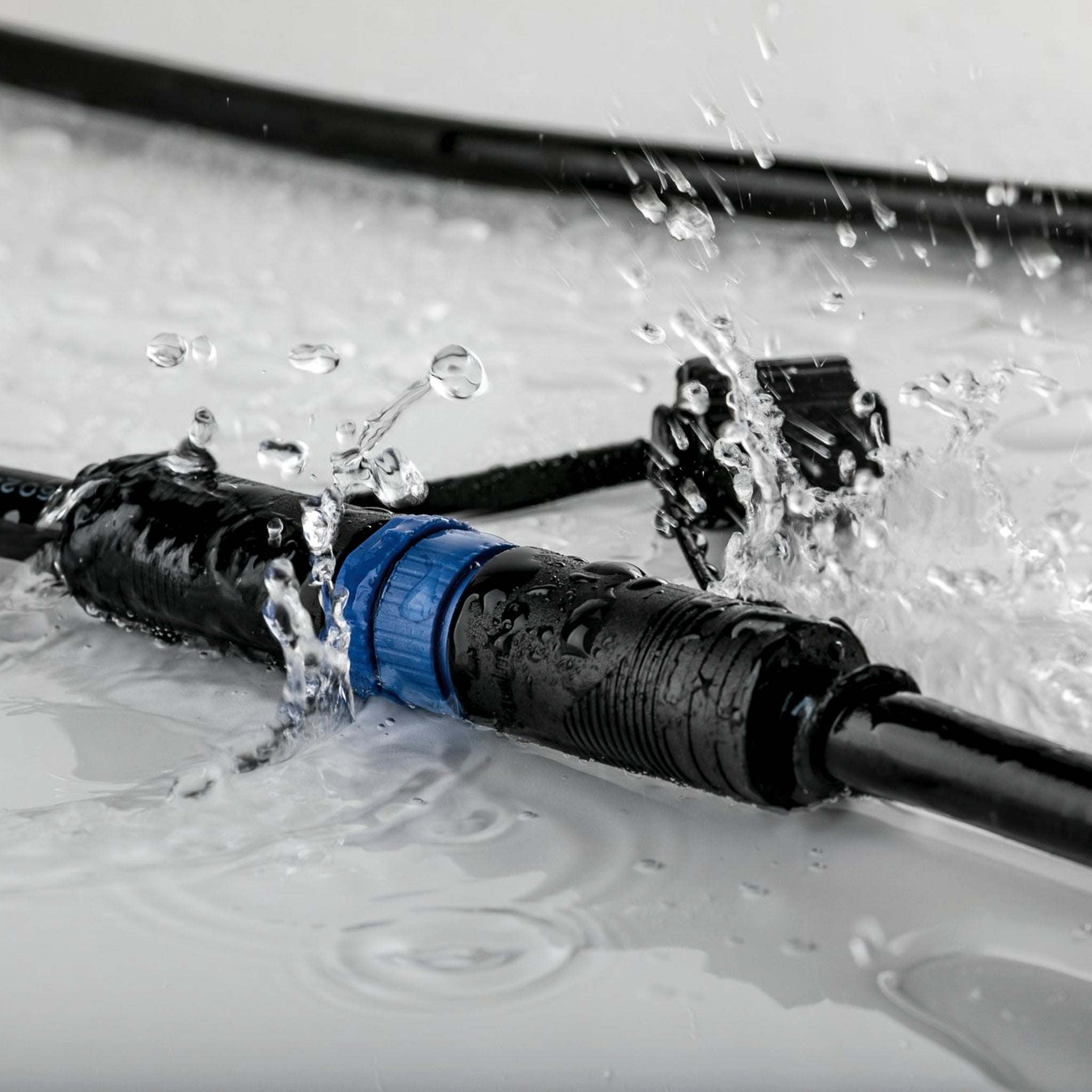 Close-up of the Paulmann - Plug & Shine Outdoor Pike 4.5W LED Warm White Individual Spotlight in Anthracite cables with connectors splashing in water, ideal for outdoor lighting installations.