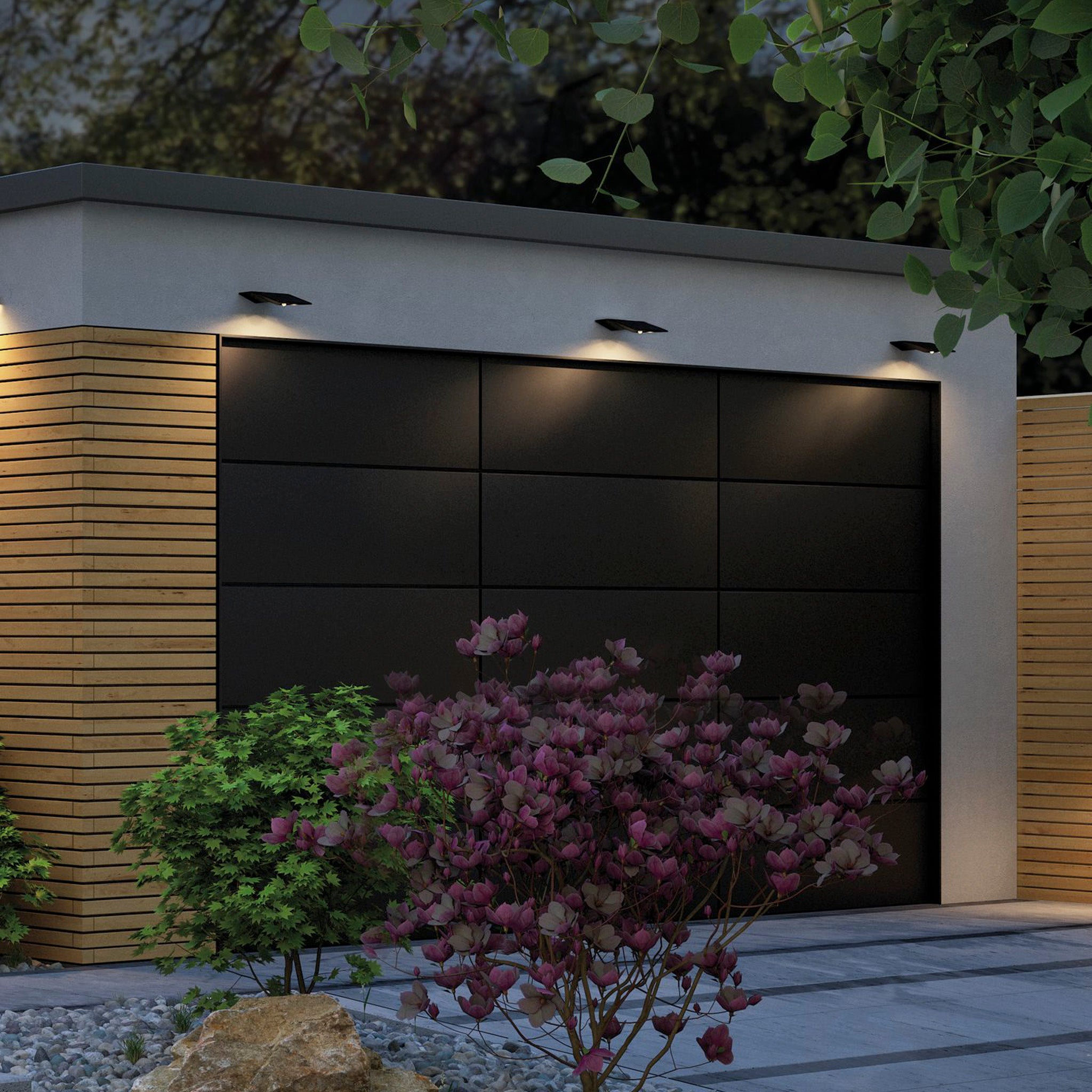 A modern garage with a black door is surrounded by wooden paneling and purple flowering shrubs, illuminated by the Paulmann Outdoor Yoko 1.2W LED House Number Wall Lumination Light in anthracite, featuring motion detection.